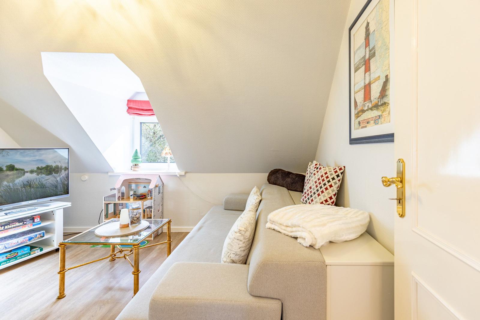 Living room with sofa, TV, and dollhouse under sloped ceiling.