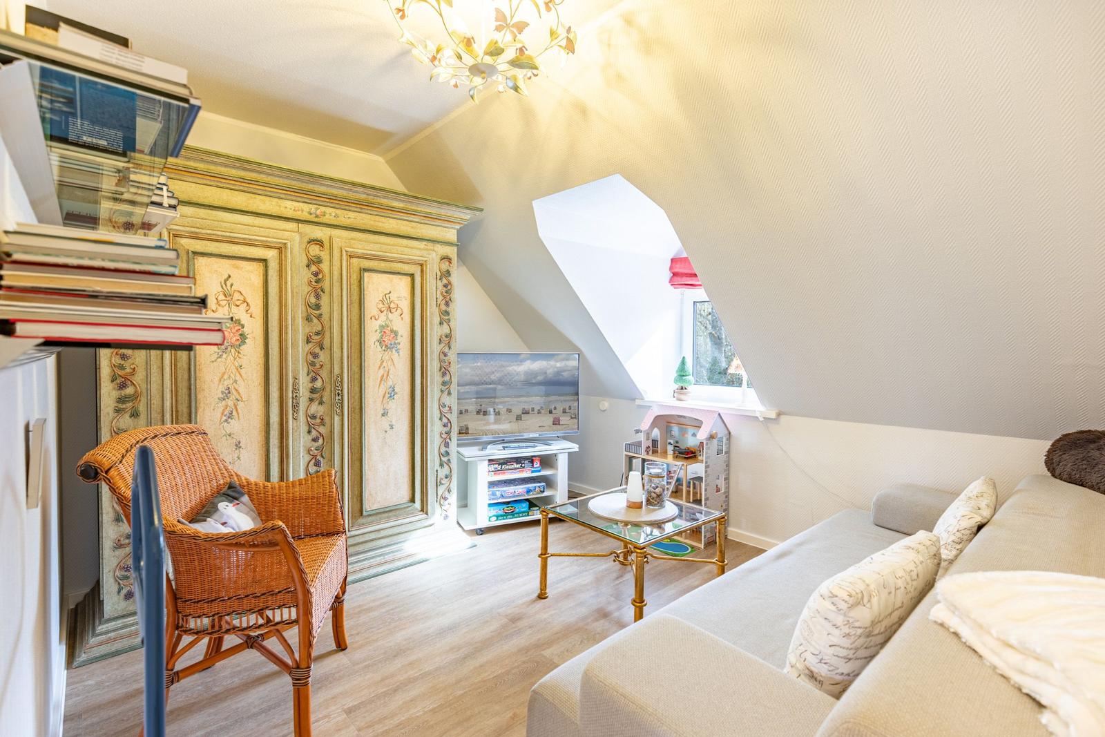 Living room with sofa, TV, and decorative cabinet under sloped ceiling