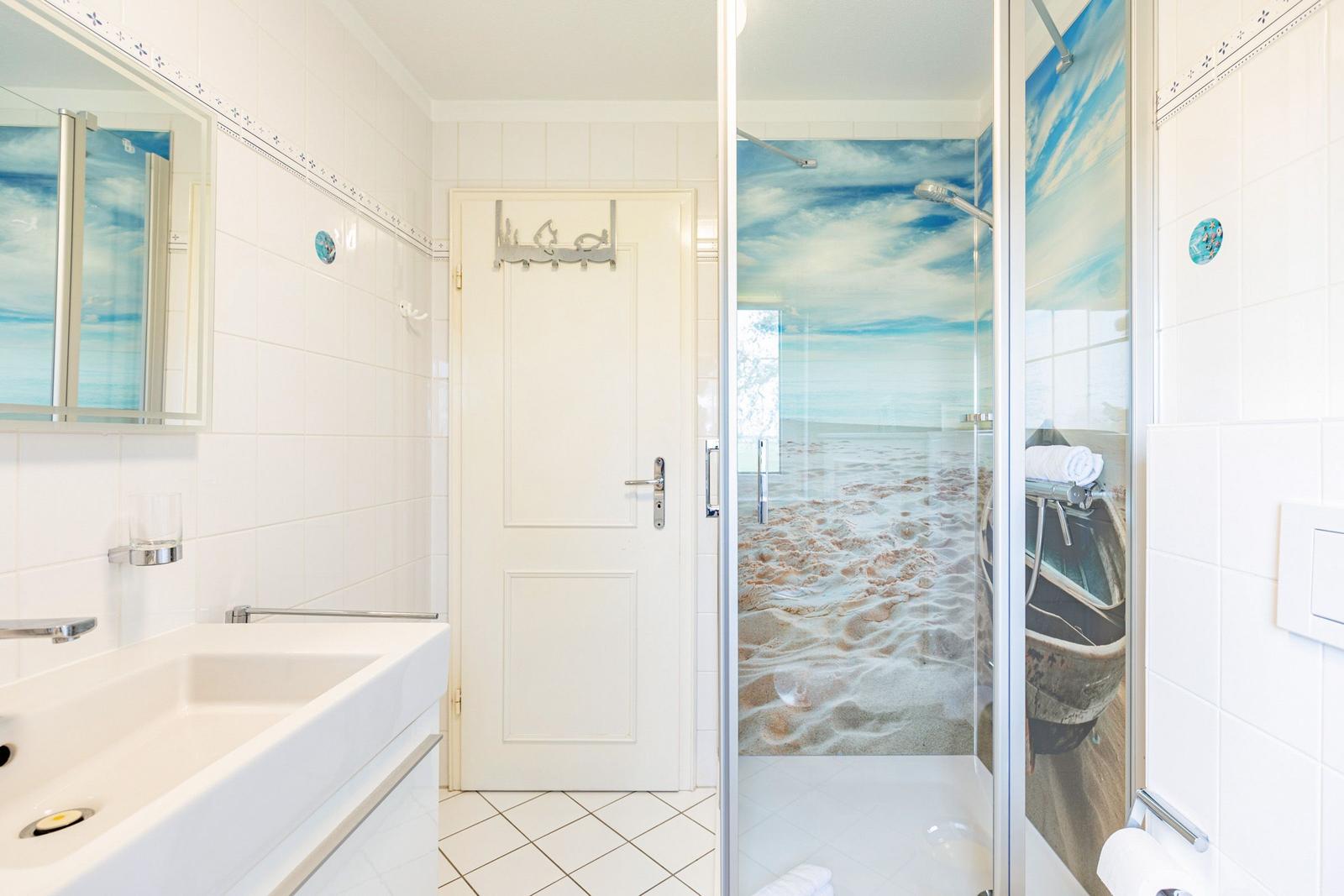 Bathroom with shower, mirror, and sink. Shower wall shows beach motif.