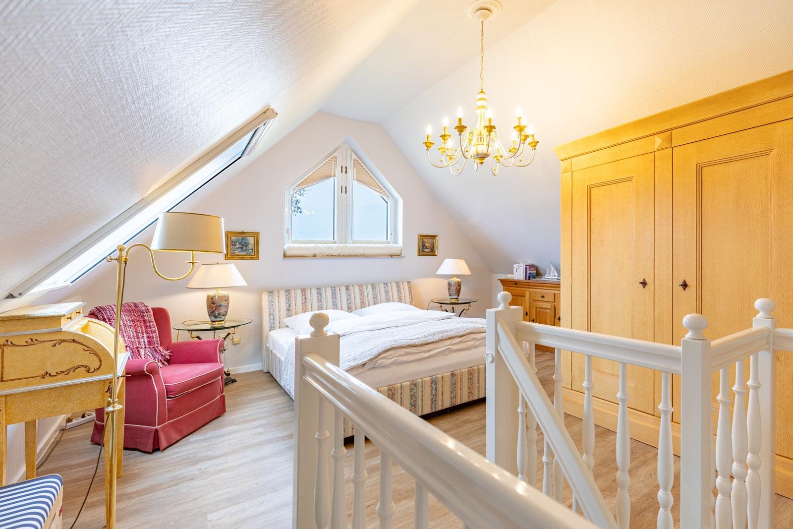 Bedroom with sloped ceiling, bed, wardrobe, and seating area.