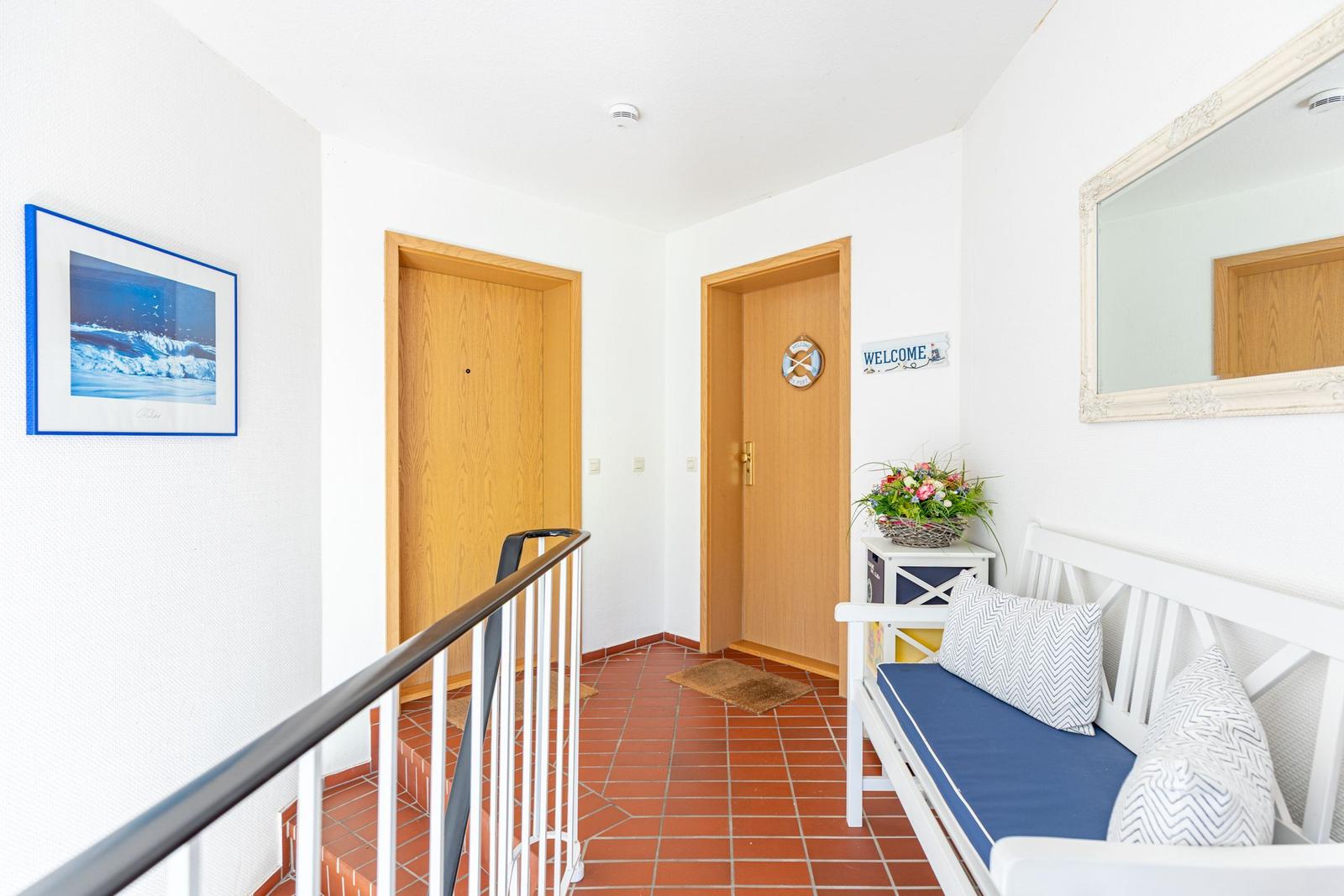 Hallway with wooden doors, red tiled floor, and white sofa with cushions.