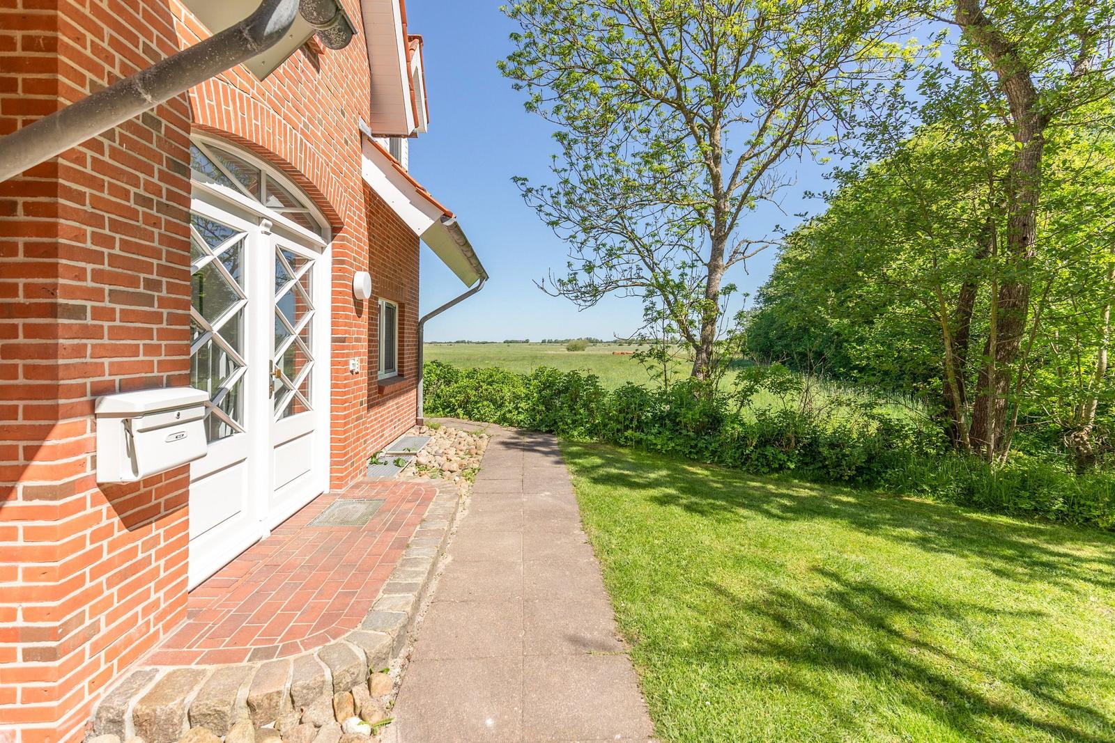 Red brick house with white doors. Path leads through meadow to a forest.