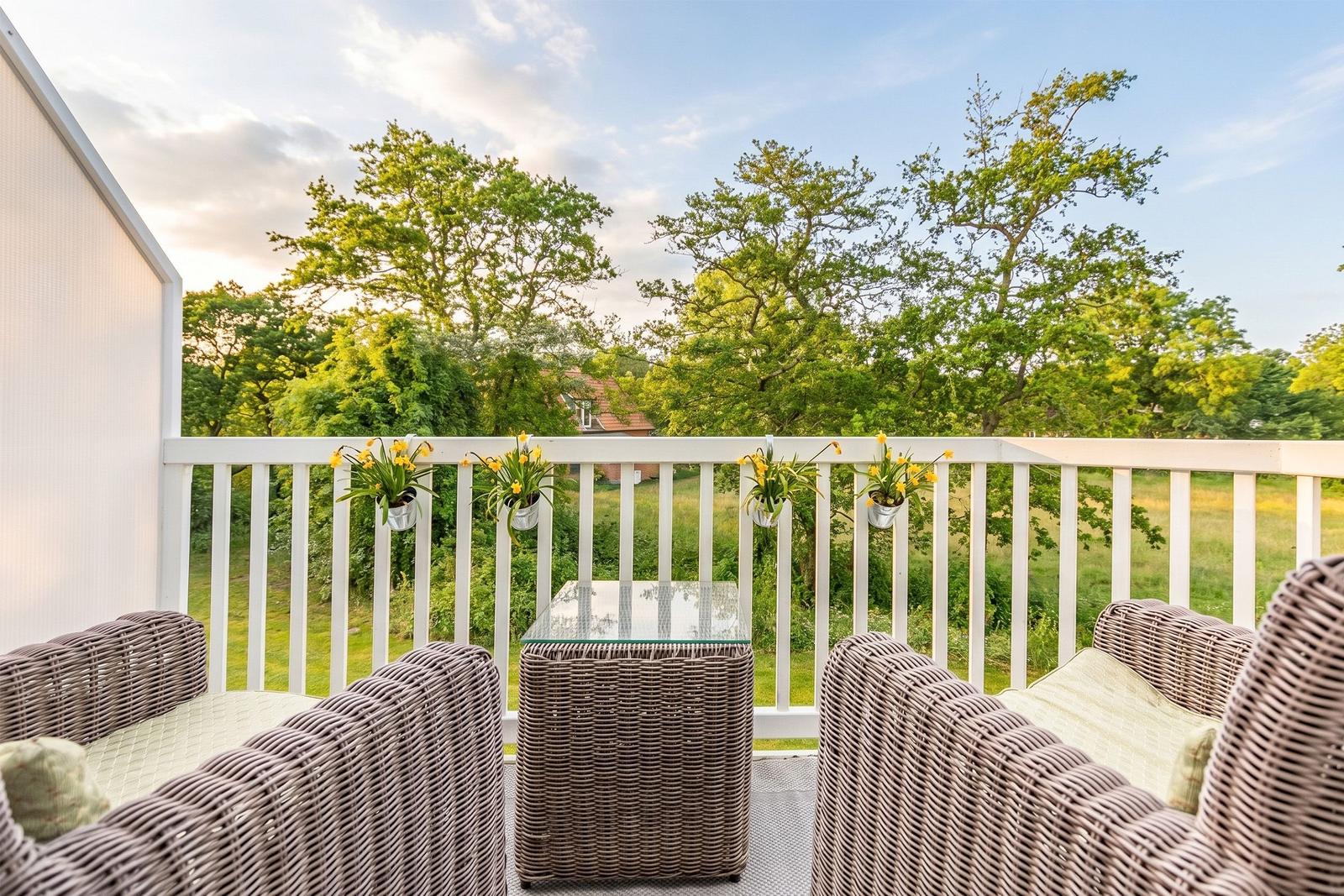 Terrace with wicker furniture and hanging planters. View of green trees and a garden.