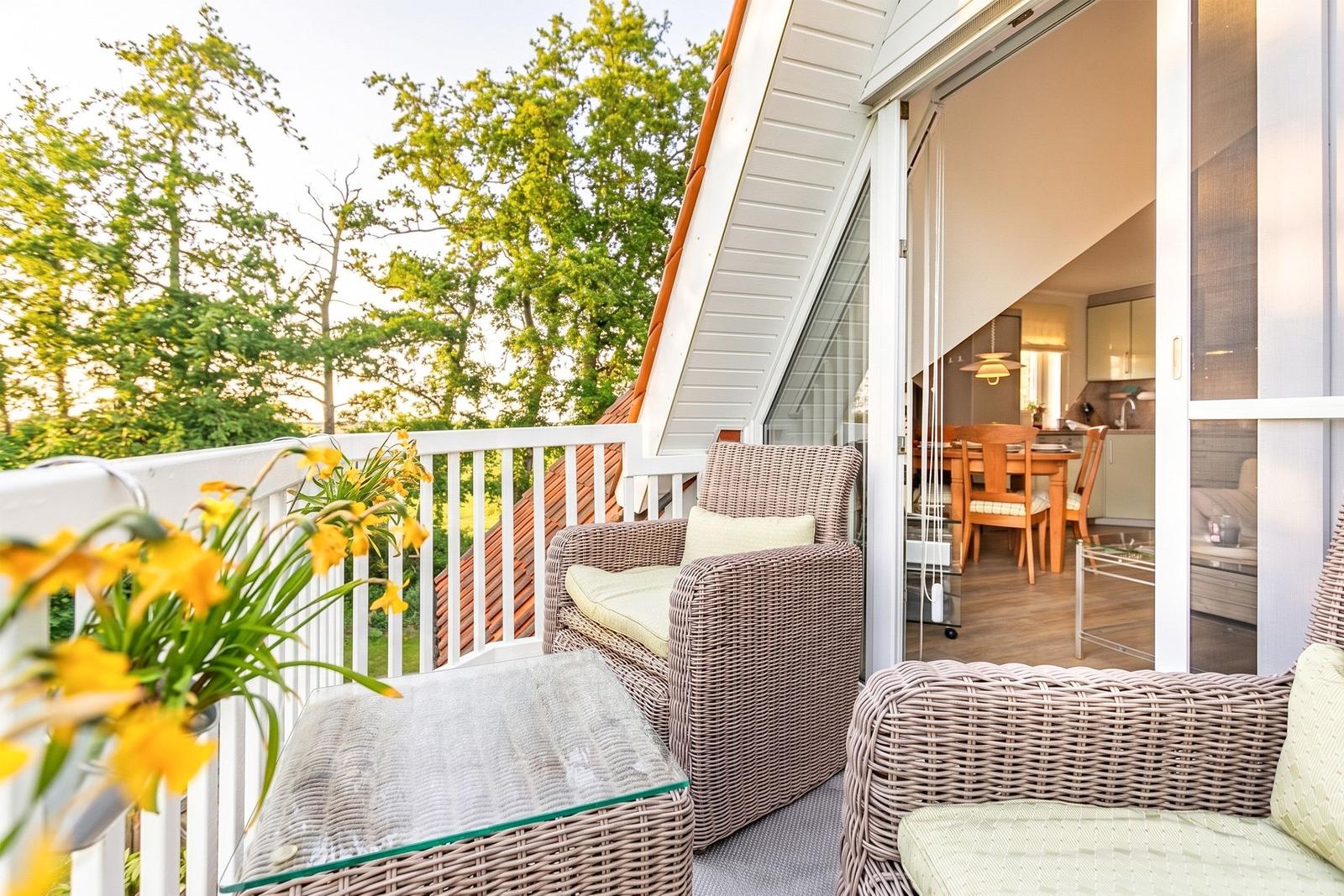 Terrace with wicker furniture and view of green trees. Kitchen area visible through glass wall.