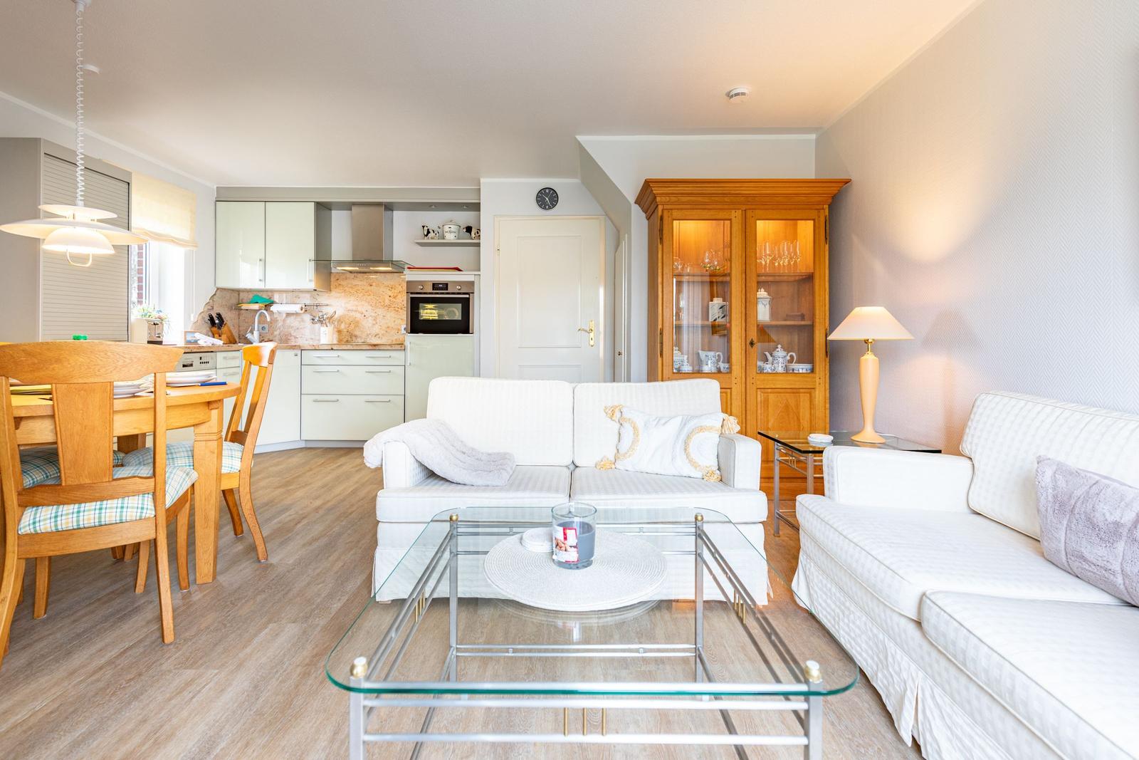 Living and dining area with kitchen. White sofas, glass table, and wooden furniture.