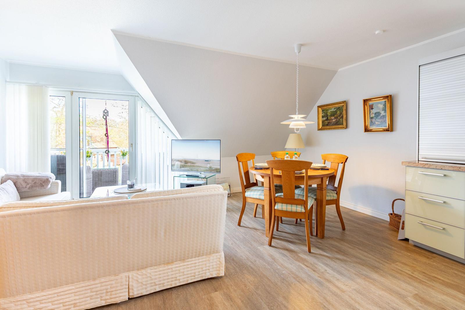 Living and dining area with wooden table, sofa, and TV. Terrace via glass doors.