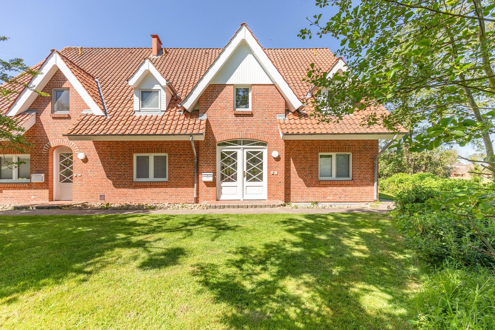 Red brick house with white window frames and dormers. Lawn and trees in the front yard.
