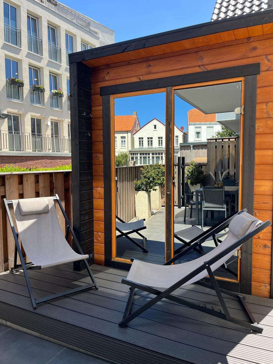 Terrace with two lounge chairs and glass doors to the garden view.
