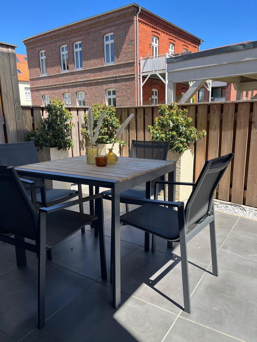 Terrace with table and chairs, surrounded by plants and wooden fence.