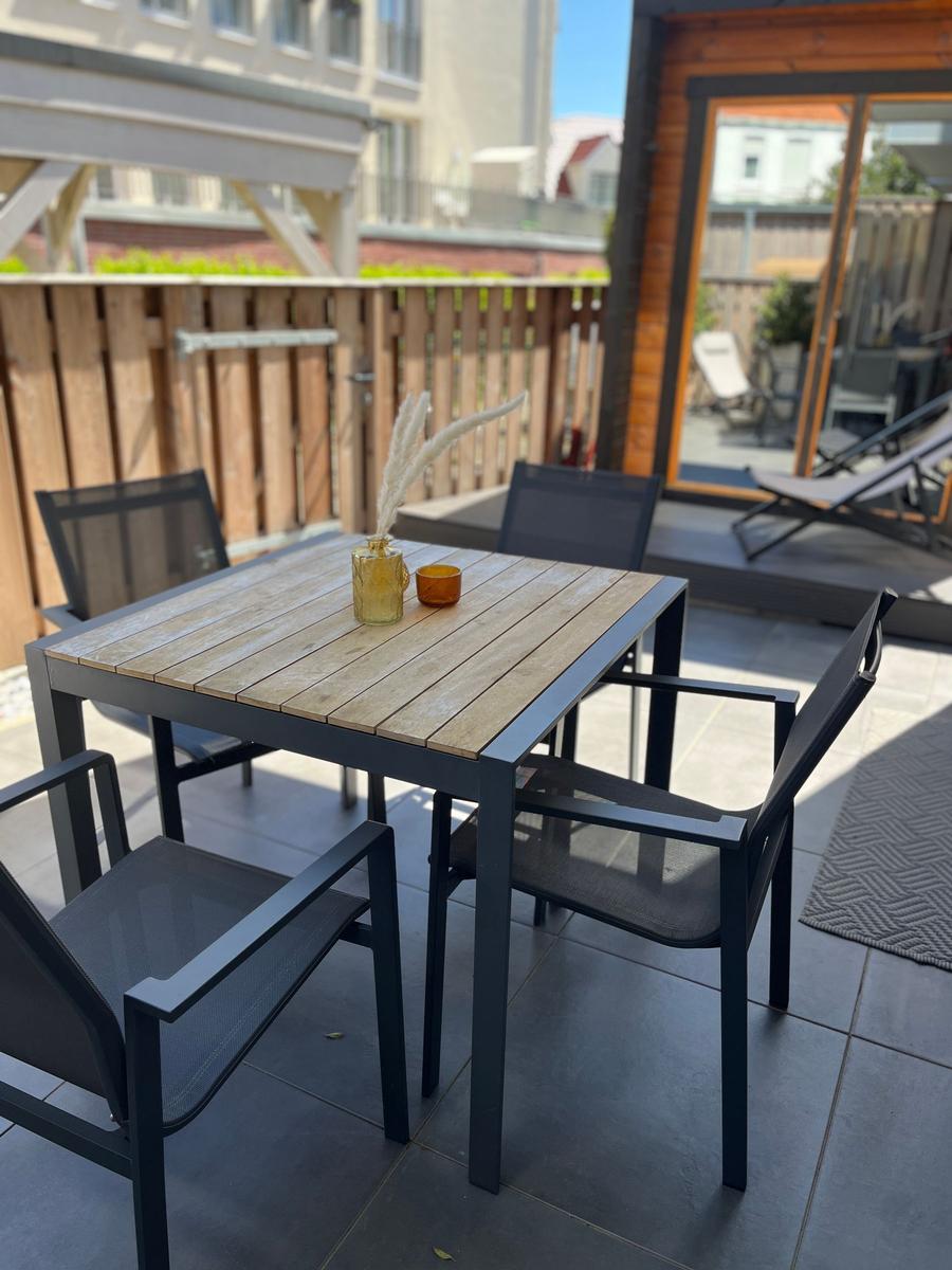 Terrace with table and chairs, wooden top, glass vases, sunlight.