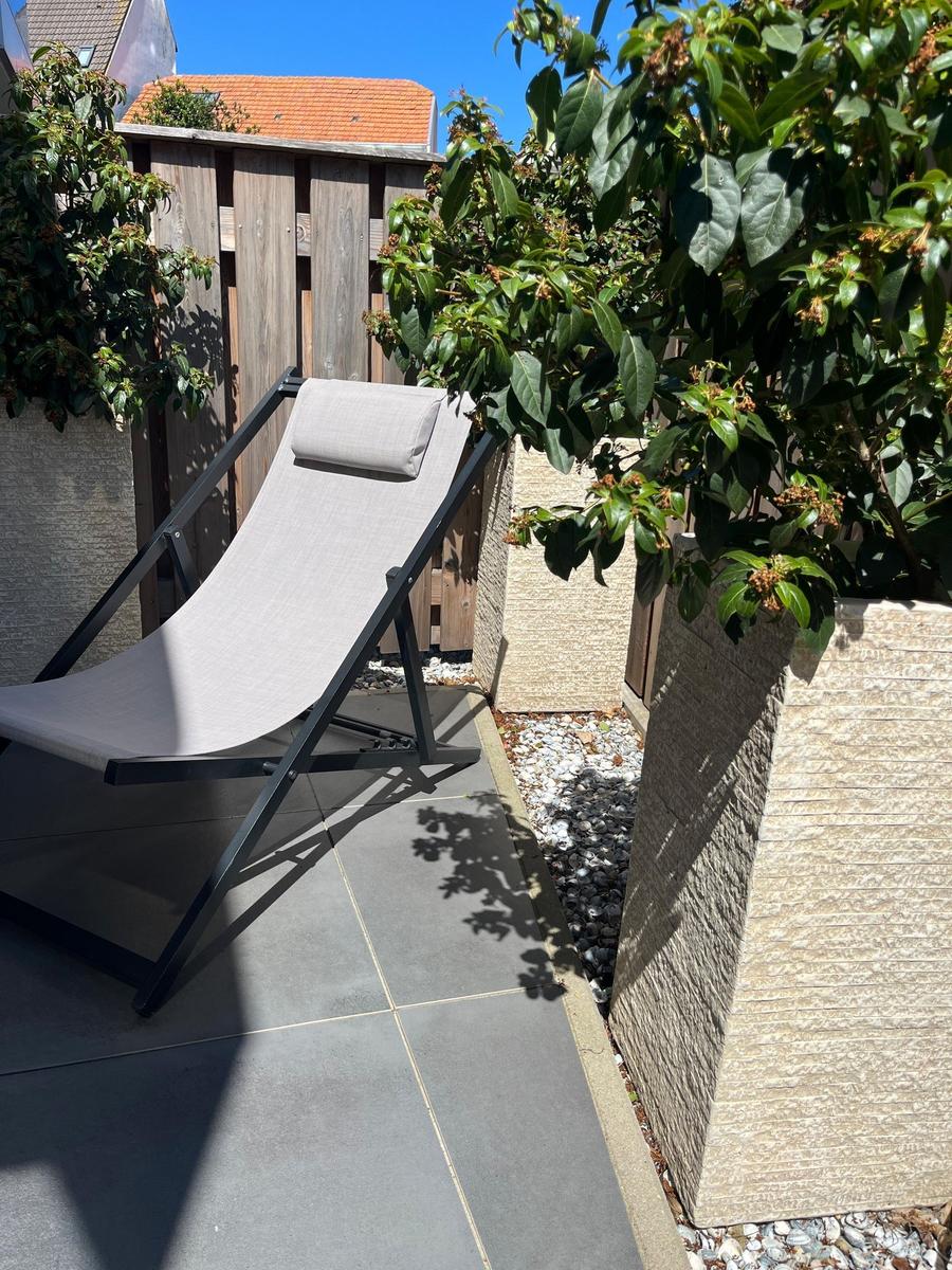 Lounger on terrace between plants and stone walls.