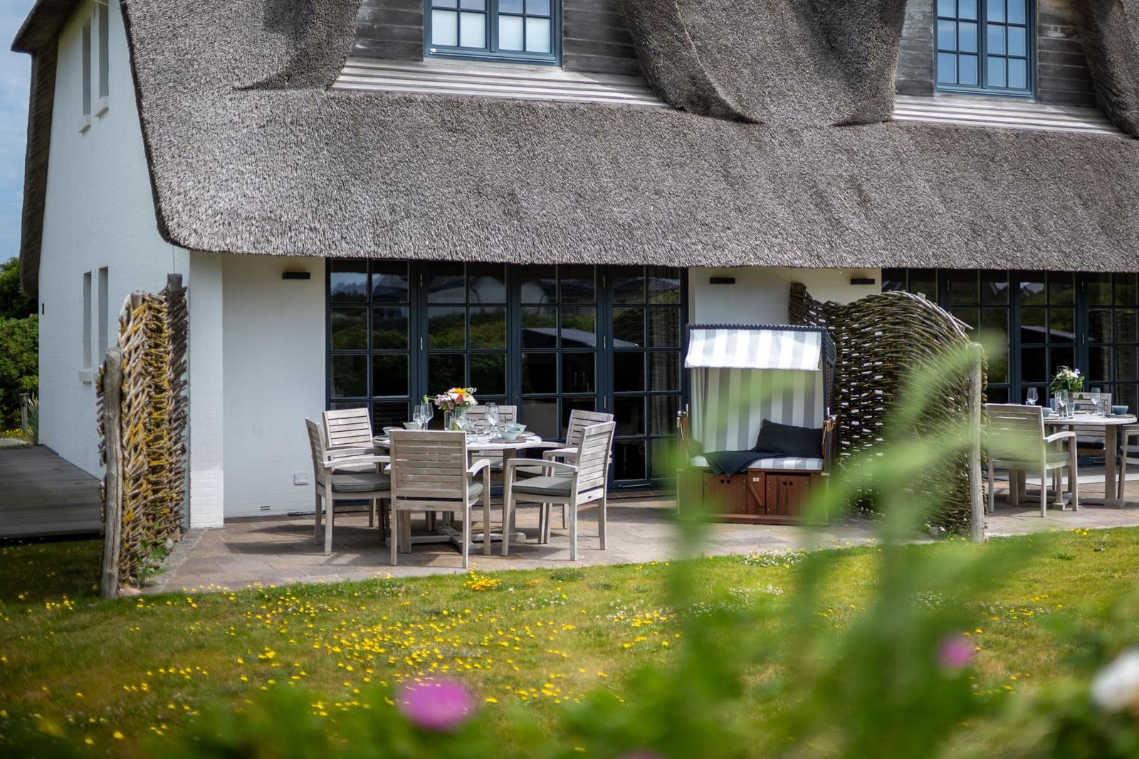 Terrace with table, chairs, and beach chair in front of a thatched-roof house.