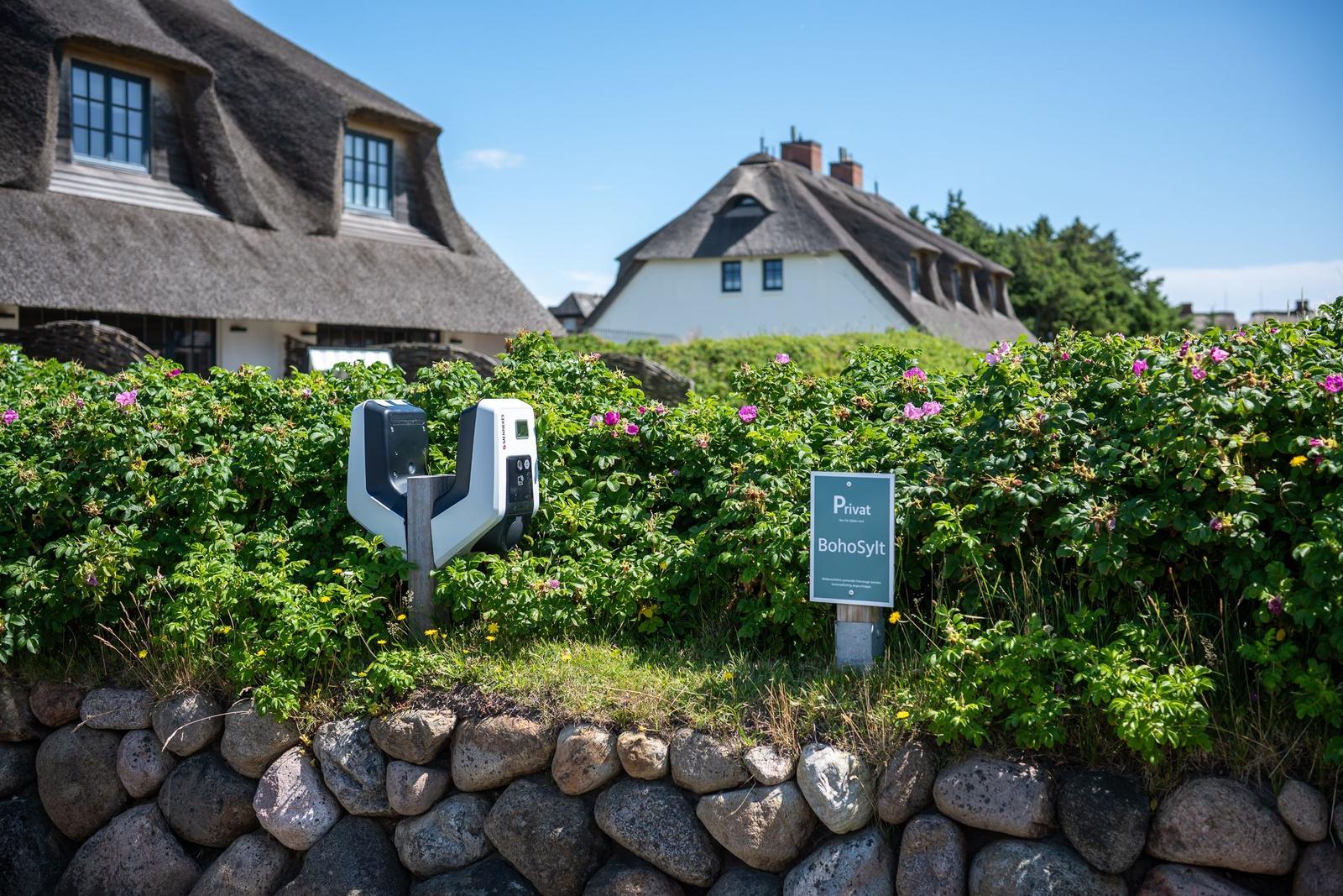 Private entrance with charging station and sign in front of traditional houses with thatched roofs.