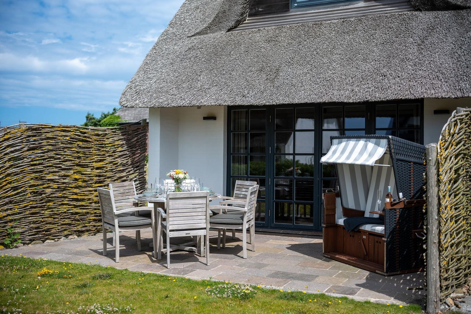 Terrace with table, chairs, and beach chair in front of a thatched house.
