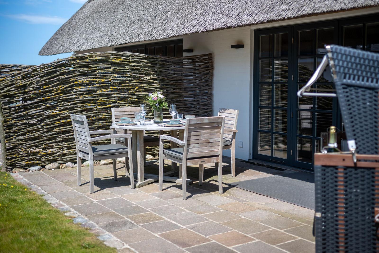 Terrasse mit Tisch und Stühlen vor einem Haus mit Strohdach und Holzumrandung.