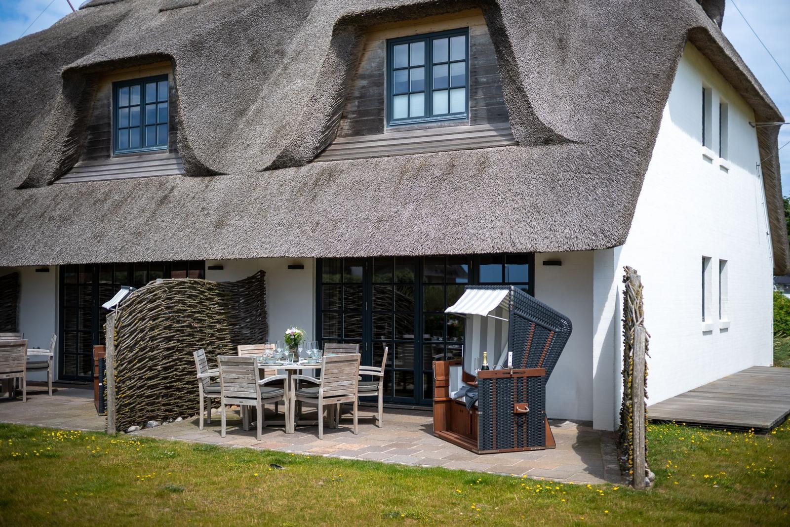Haus mit Strohdach, Terrasse mit Tisch und Stühlen, Strandkorb und Garten