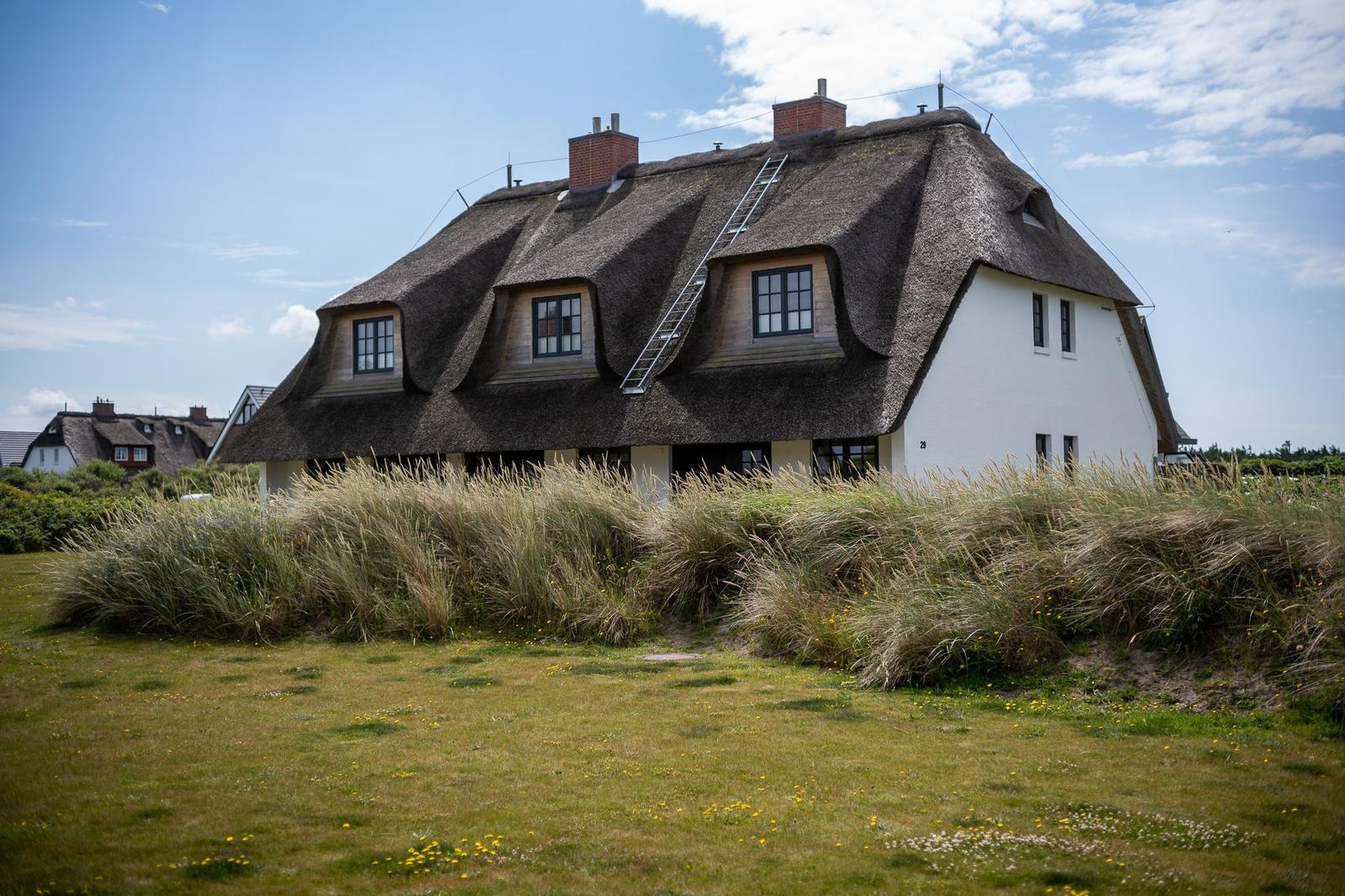 Haus mit Strohdach und Fenstern, umgeben von Gras und blauem Himmel.