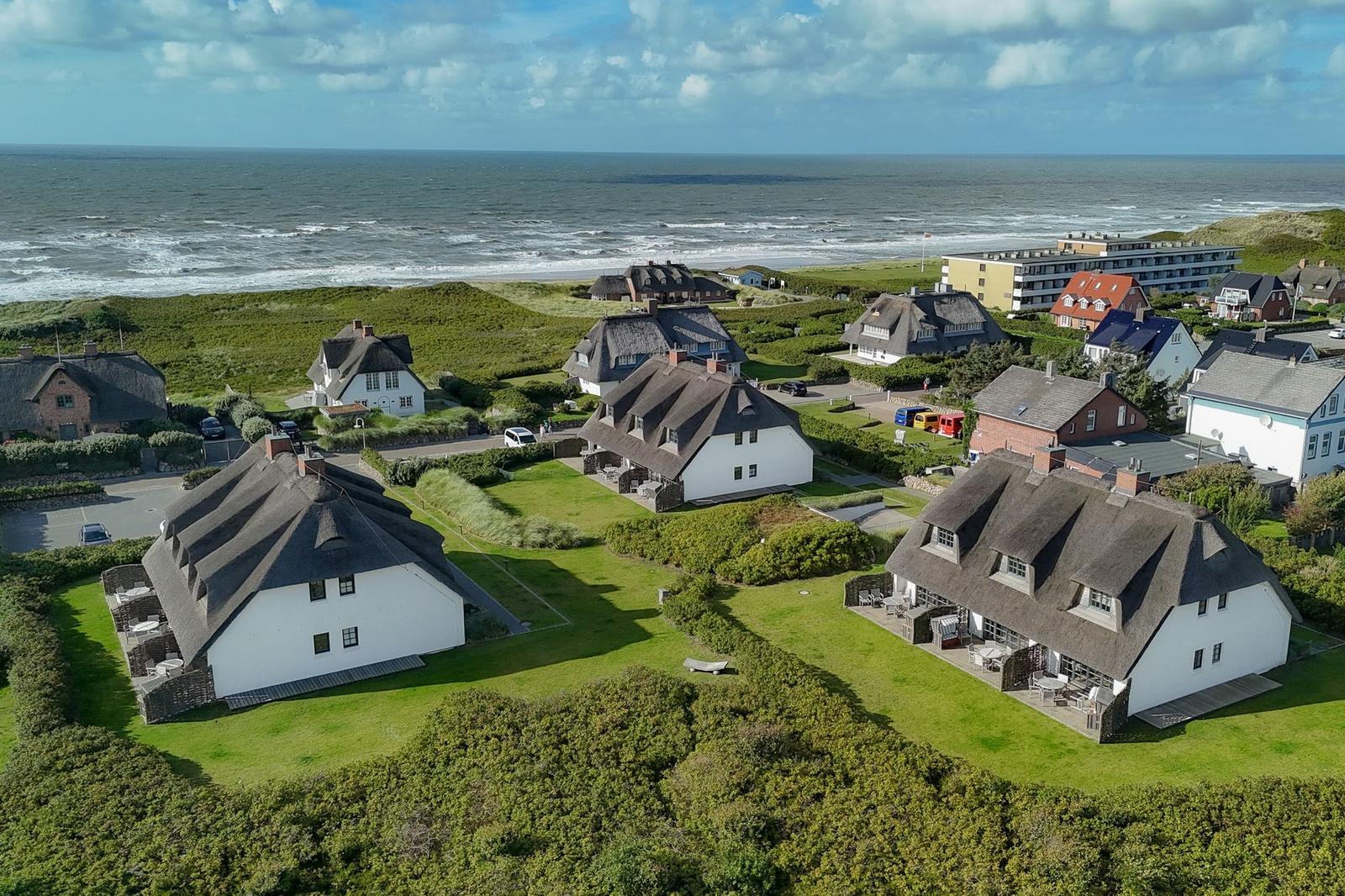 Dorfhäuser mit Strohdächern am Strand. Grünflächen und Meer im Hintergrund.