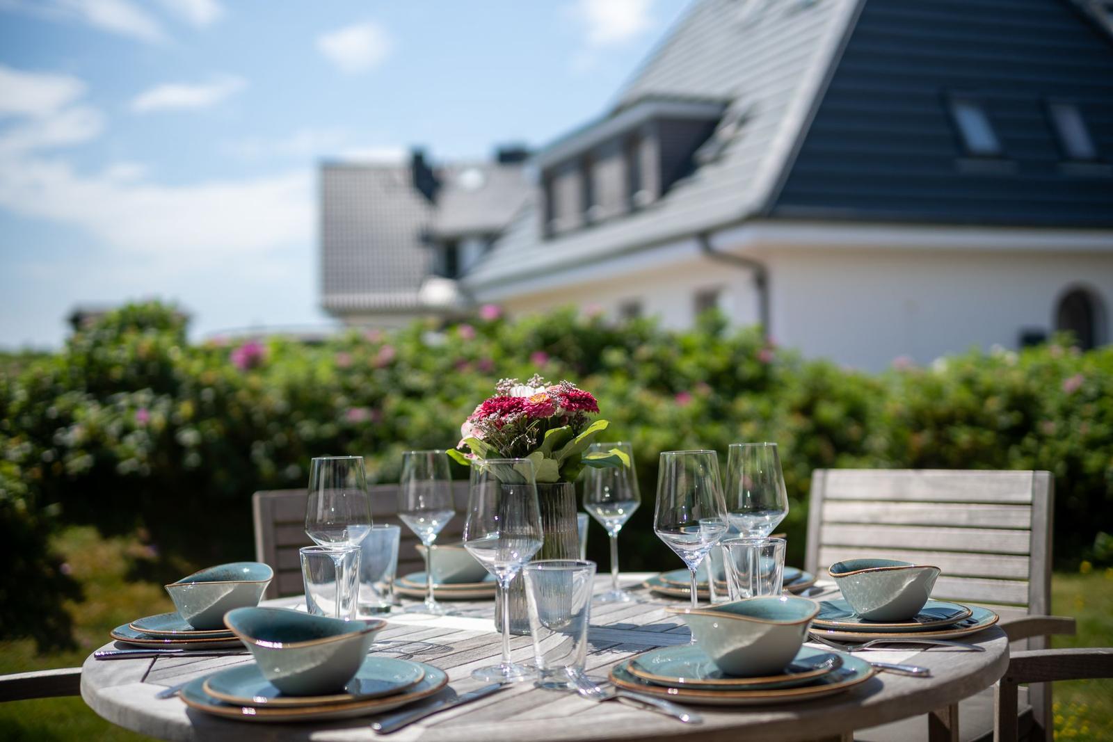 Garten-Tisch mit Geschirr und Blumen vor Haus