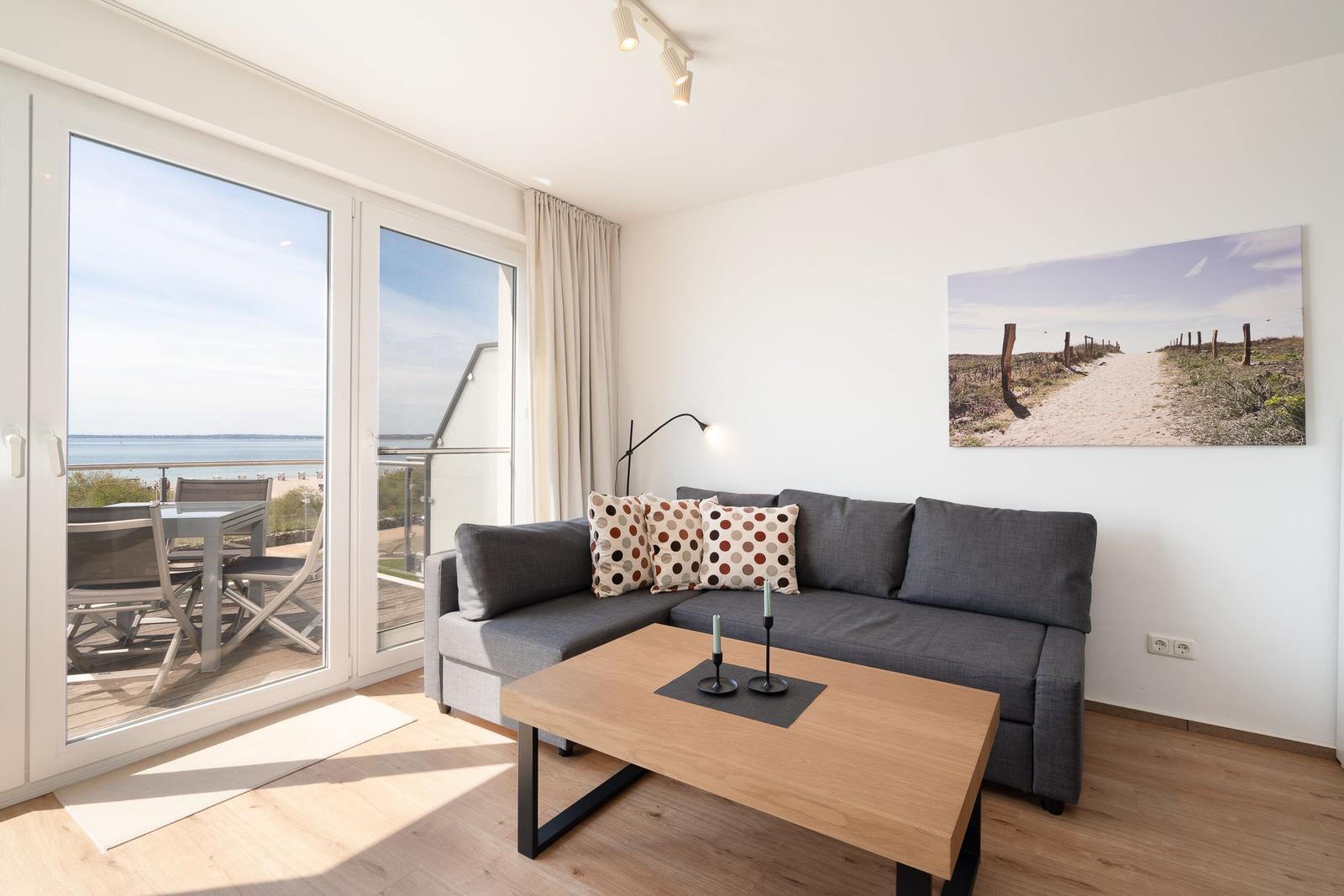 Wohnzimmer mit Sofa, Tisch und Blick auf den Strand.