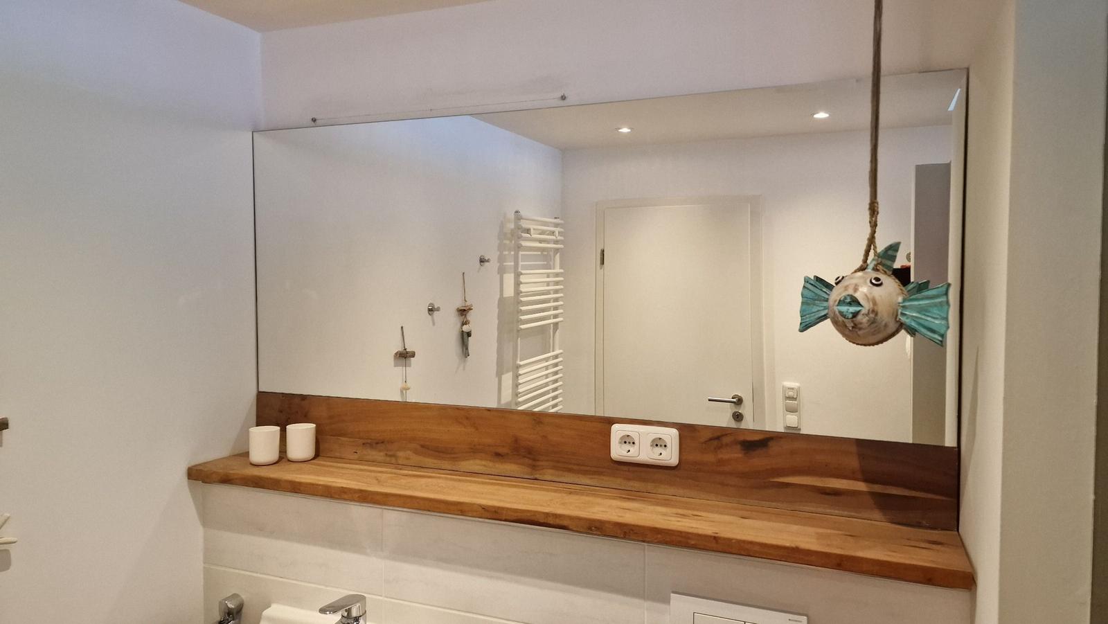 Badezimmer mit Holzwaschbecken und Spiegel. An der Wand hängt ein Fischobjekt.