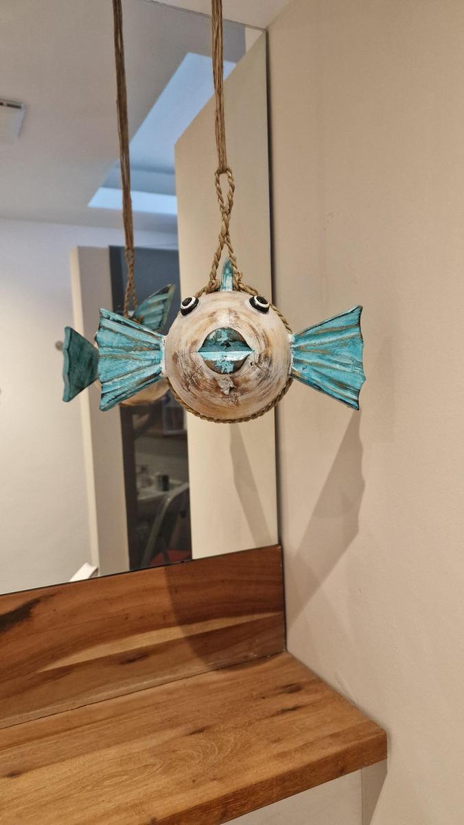 Ein hängendes Fisch-Objekt mit blauen Flossen und Augen hängt über einem Holzregal.