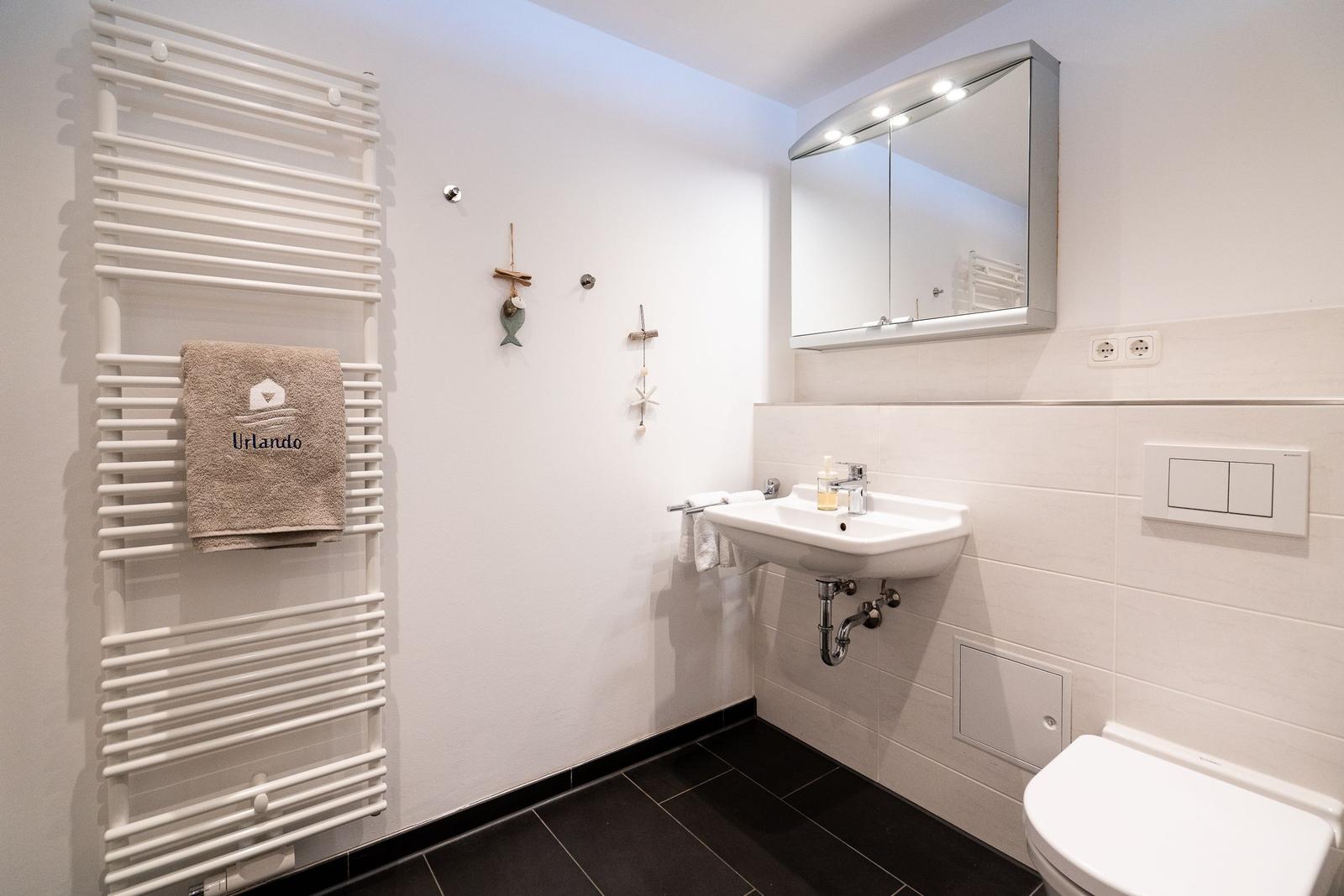 Badezimmer mit Handtuchheizkörper, Waschbecken und Spiegelschrank.
