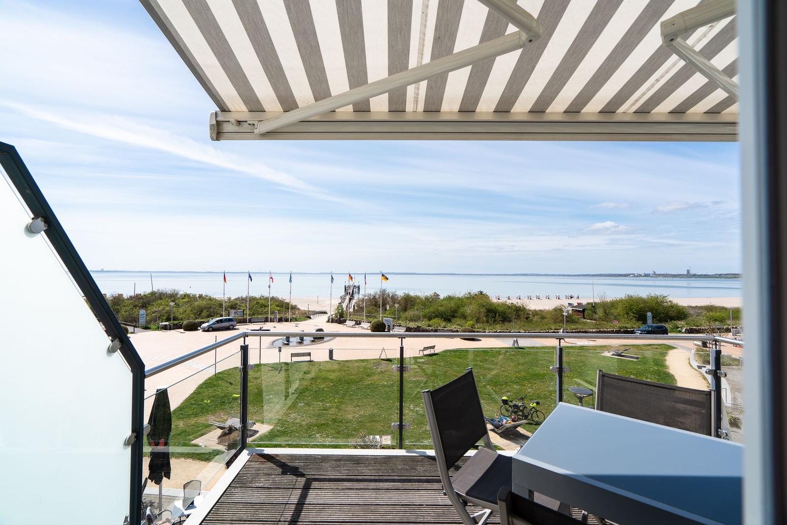 Terrasse mit Blick auf Strand und See unter einem gestreiften Markisen.