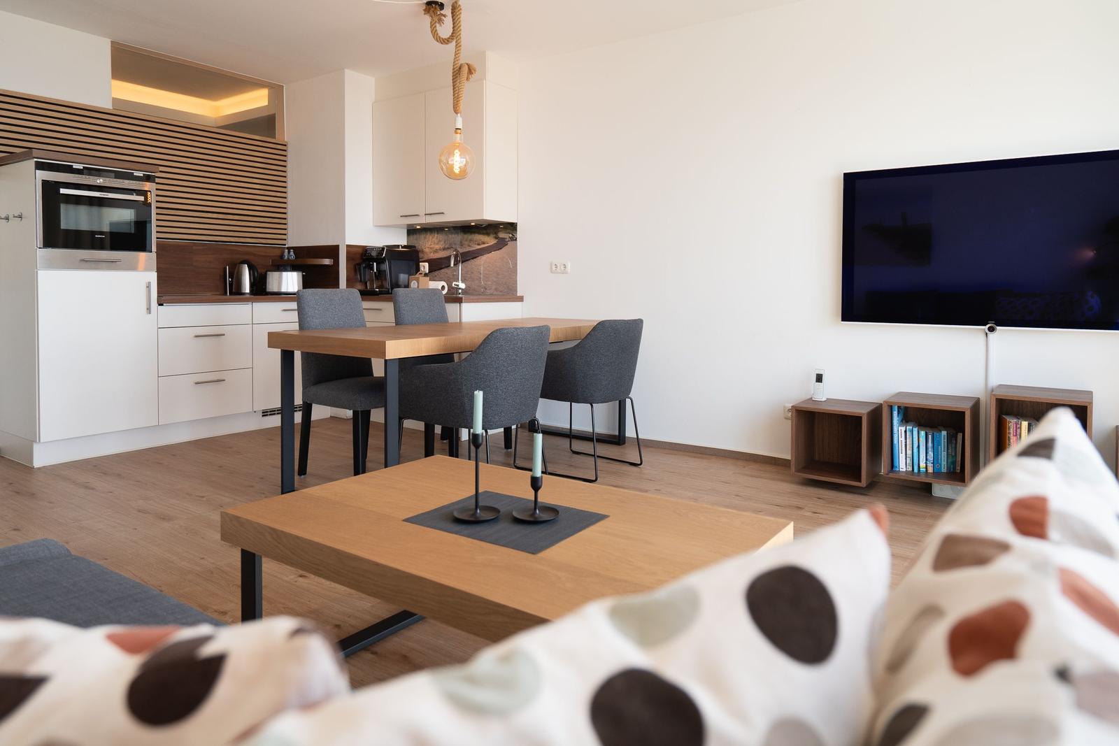 Wohn- und Essbereich mit Küchenzeile, Esstisch und Fernseher an der Wand.