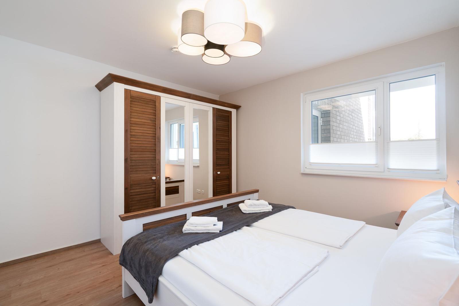 Schlafzimmer mit Doppelbett, Kleiderschrank und Fenster.