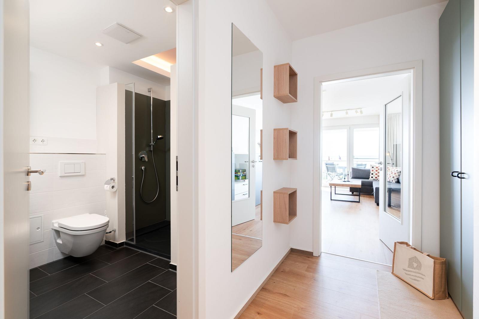 Flur mit Spiegeln und Holzregalen, Blick in Badezimmer und Wohnbereich.
