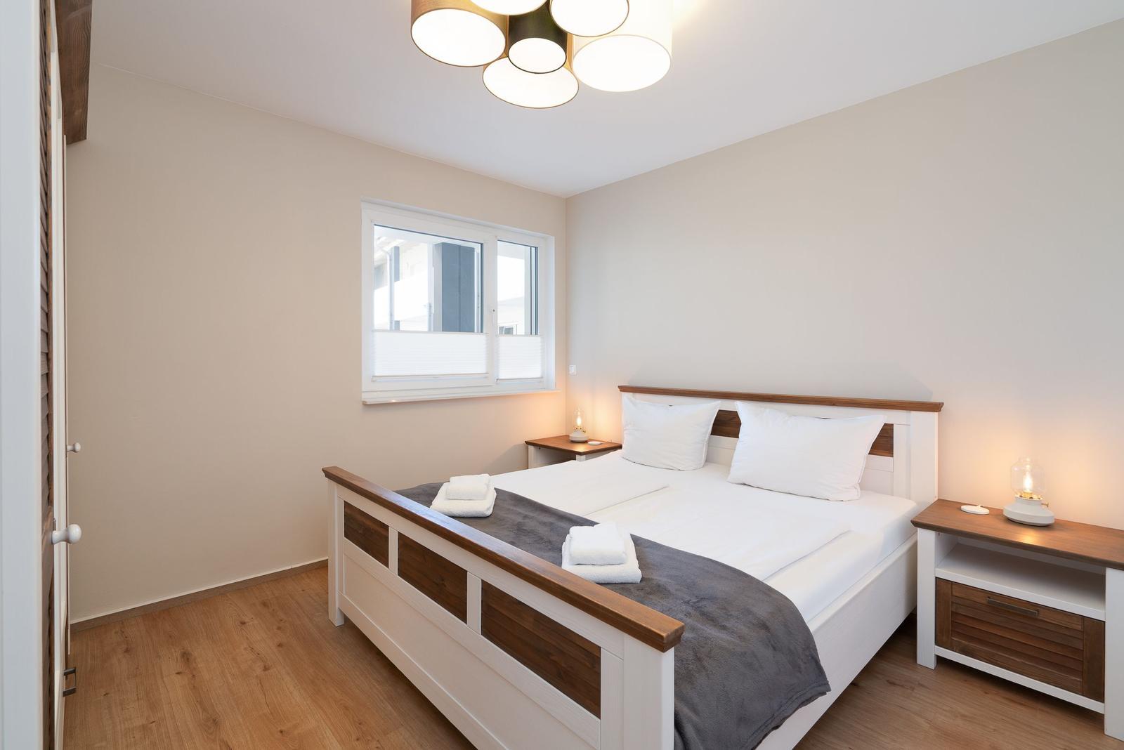 Schlafzimmer mit Bett, Nachttischen und Fenster.