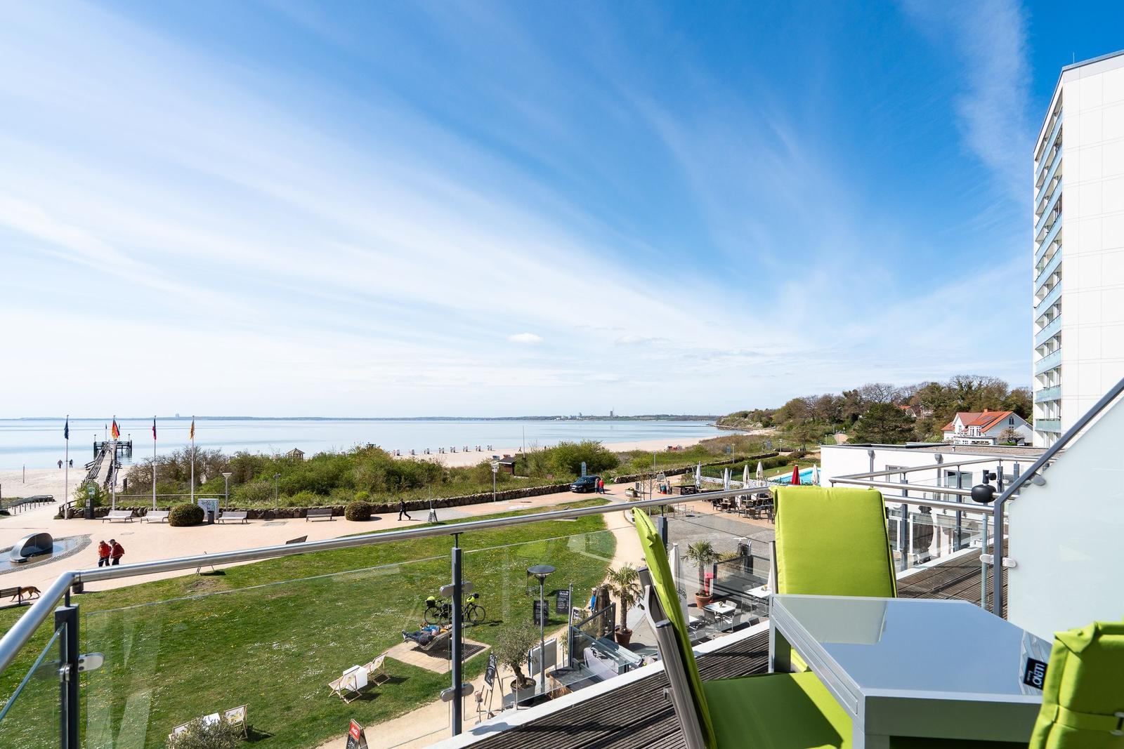 Terrasse mit grünen Stühlen und Blick auf Strand und See.