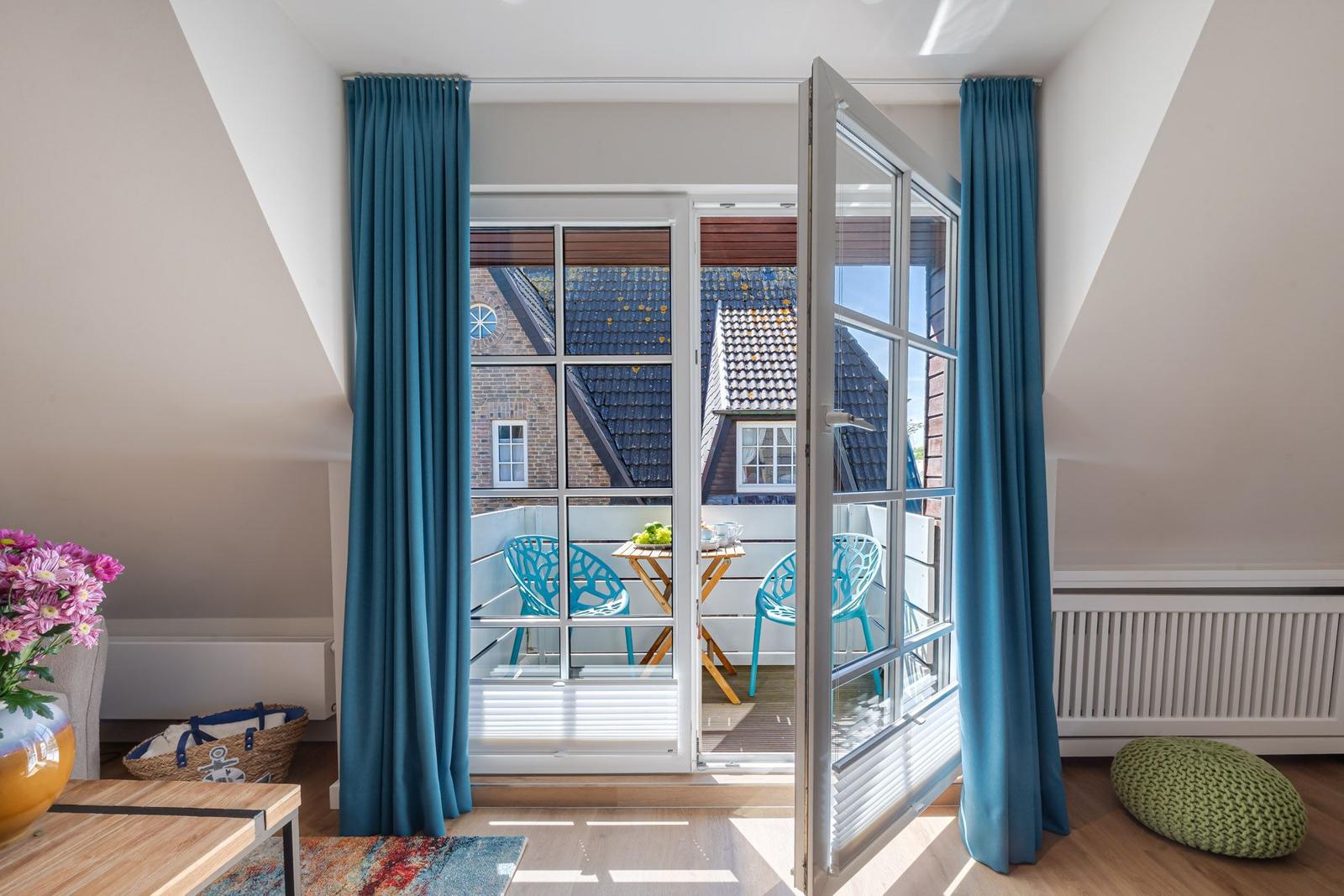 French doors with blue curtains lead to a terrace with table and chairs.