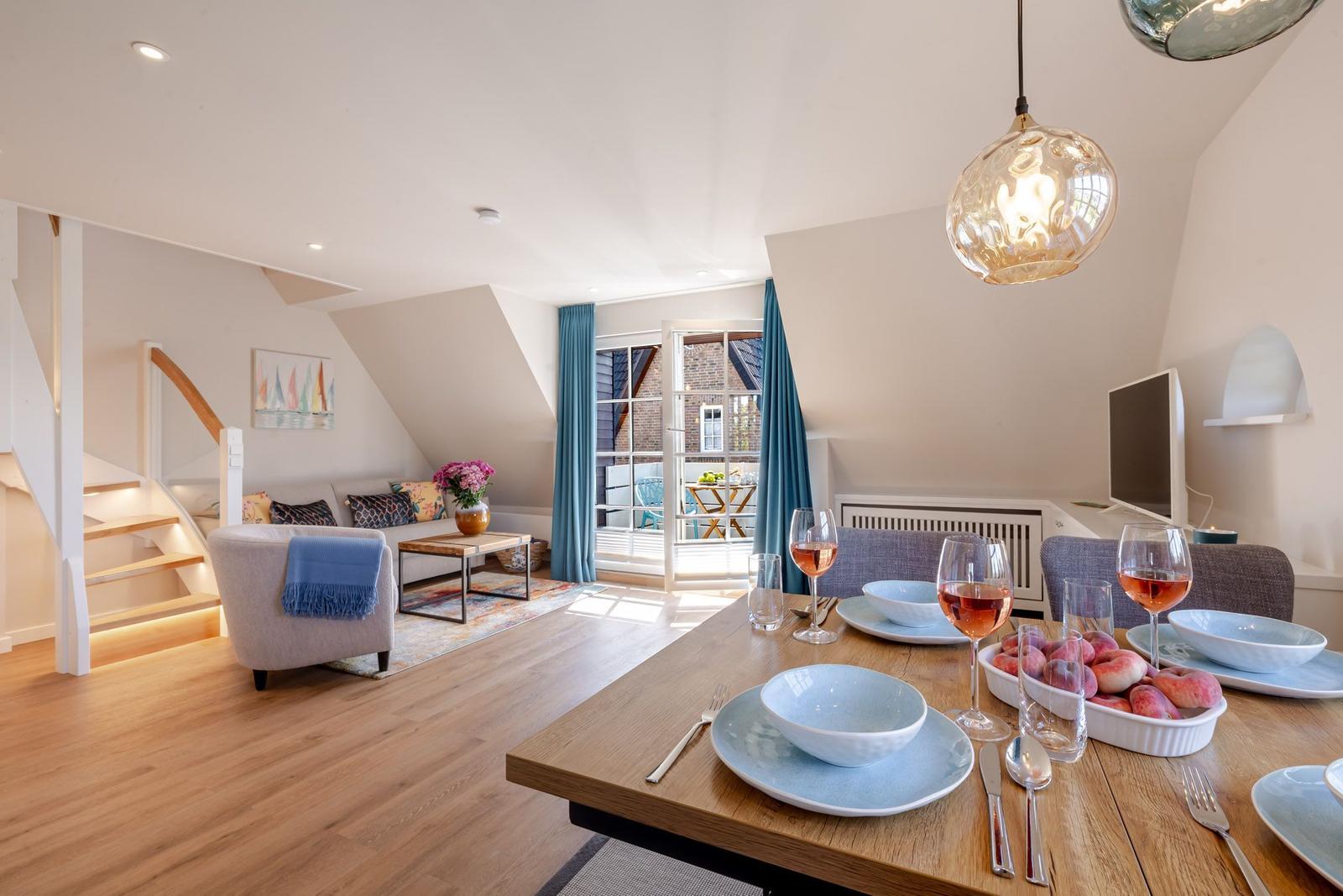 Dining area with table, chairs, and fruit. Living area with sofa, stairs, and window.