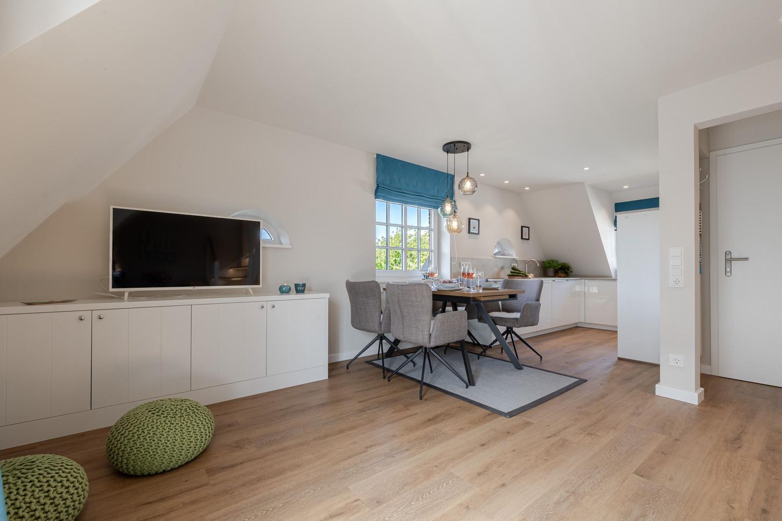 Living and dining area with TV, table and chairs, wooden floor and window with blue blinds.