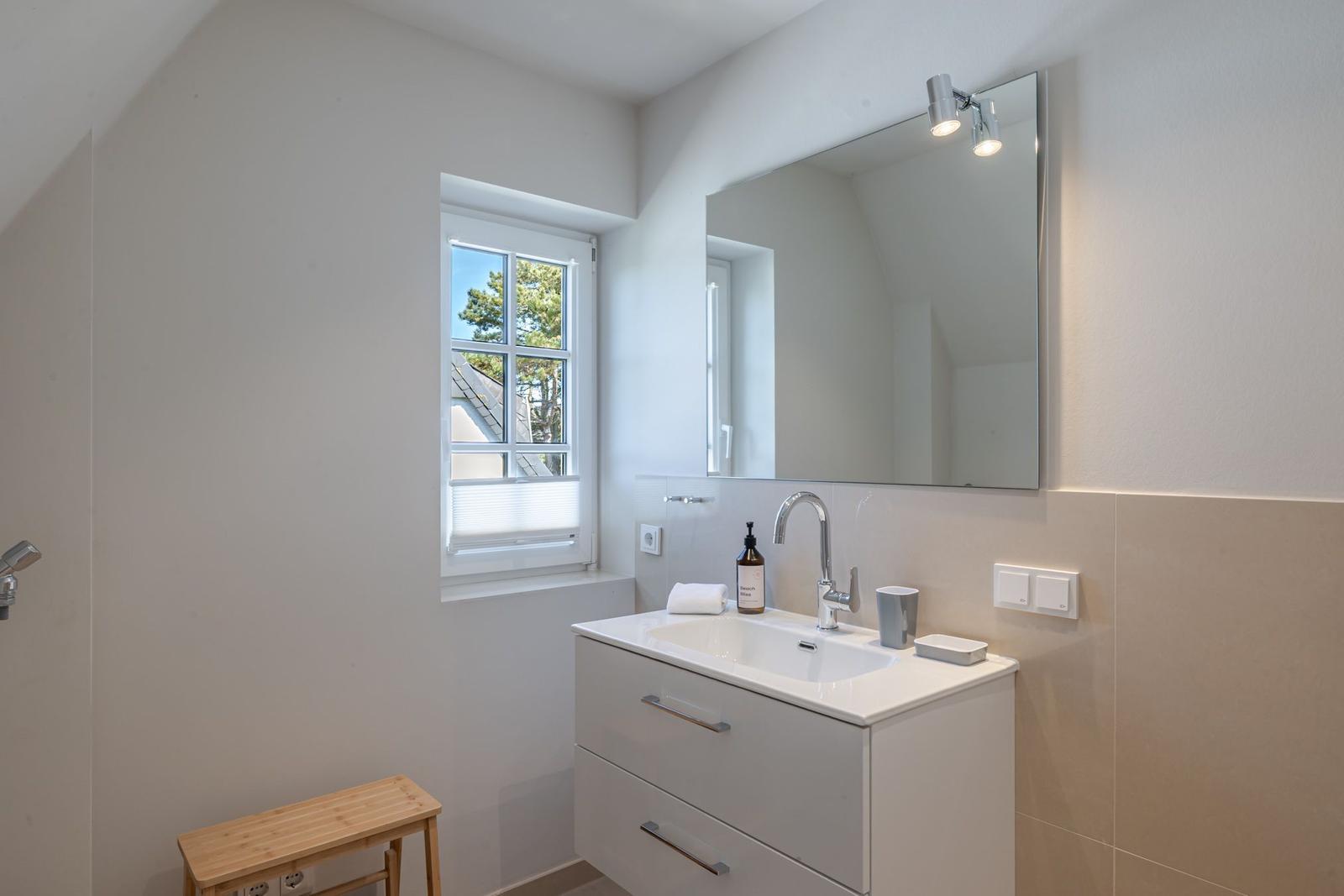 Bathroom with sink, mirror, and window. Wooden stool and shower visible.