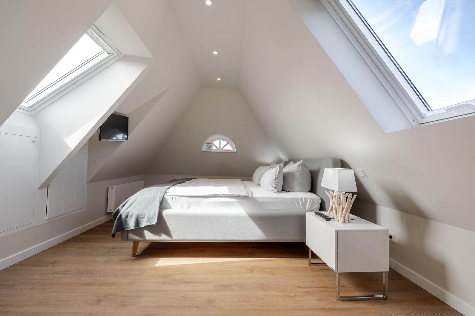 Attic room with sloped ceilings, bed, nightstand, and two skylights.