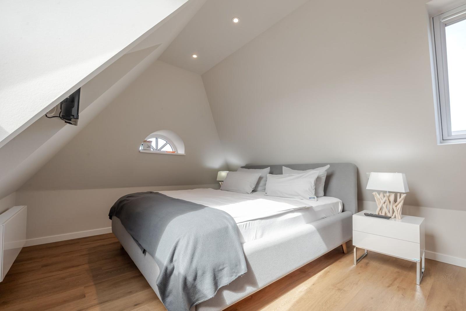 Bedroom with sloped ceiling, bed, nightstand, and window.