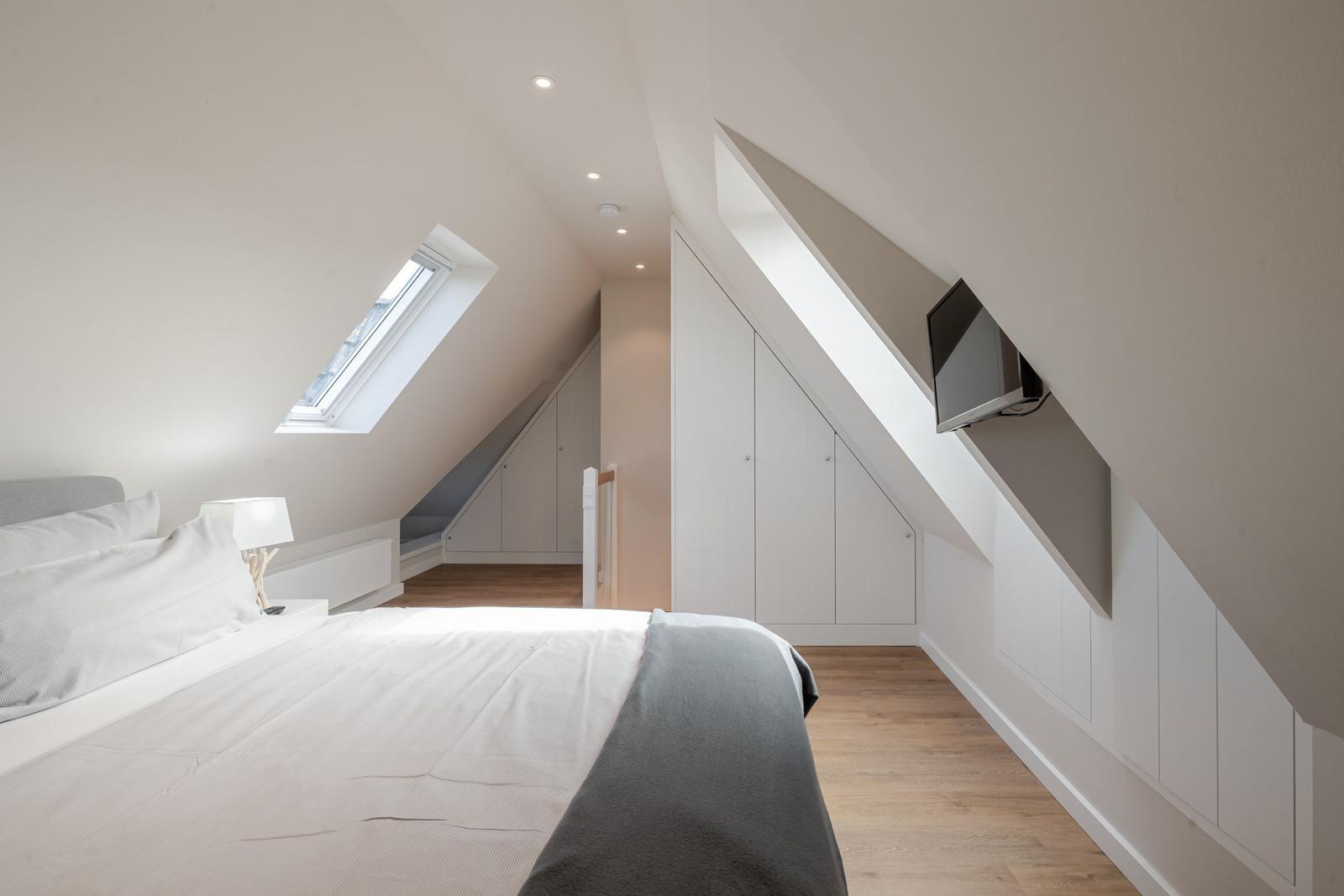 Bedroom with sloped ceiling, skylight, bed, wardrobe, and wall-mounted TV.