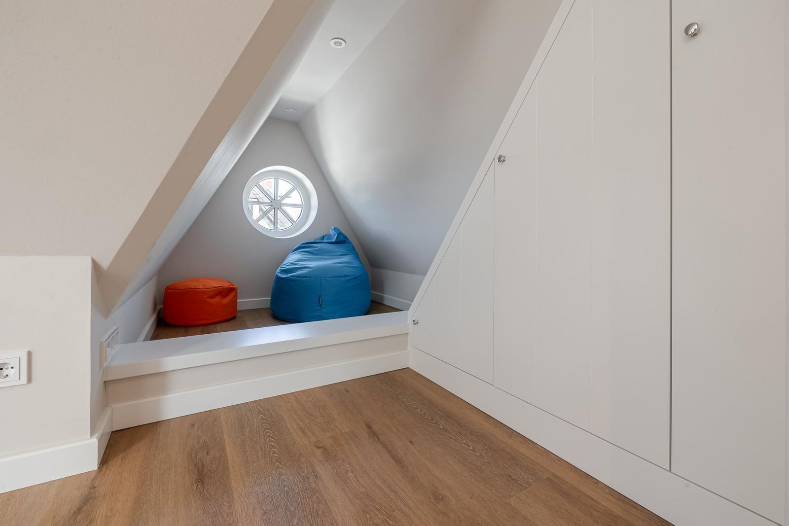 Attic room with round window, two cushions, and white cabinets.