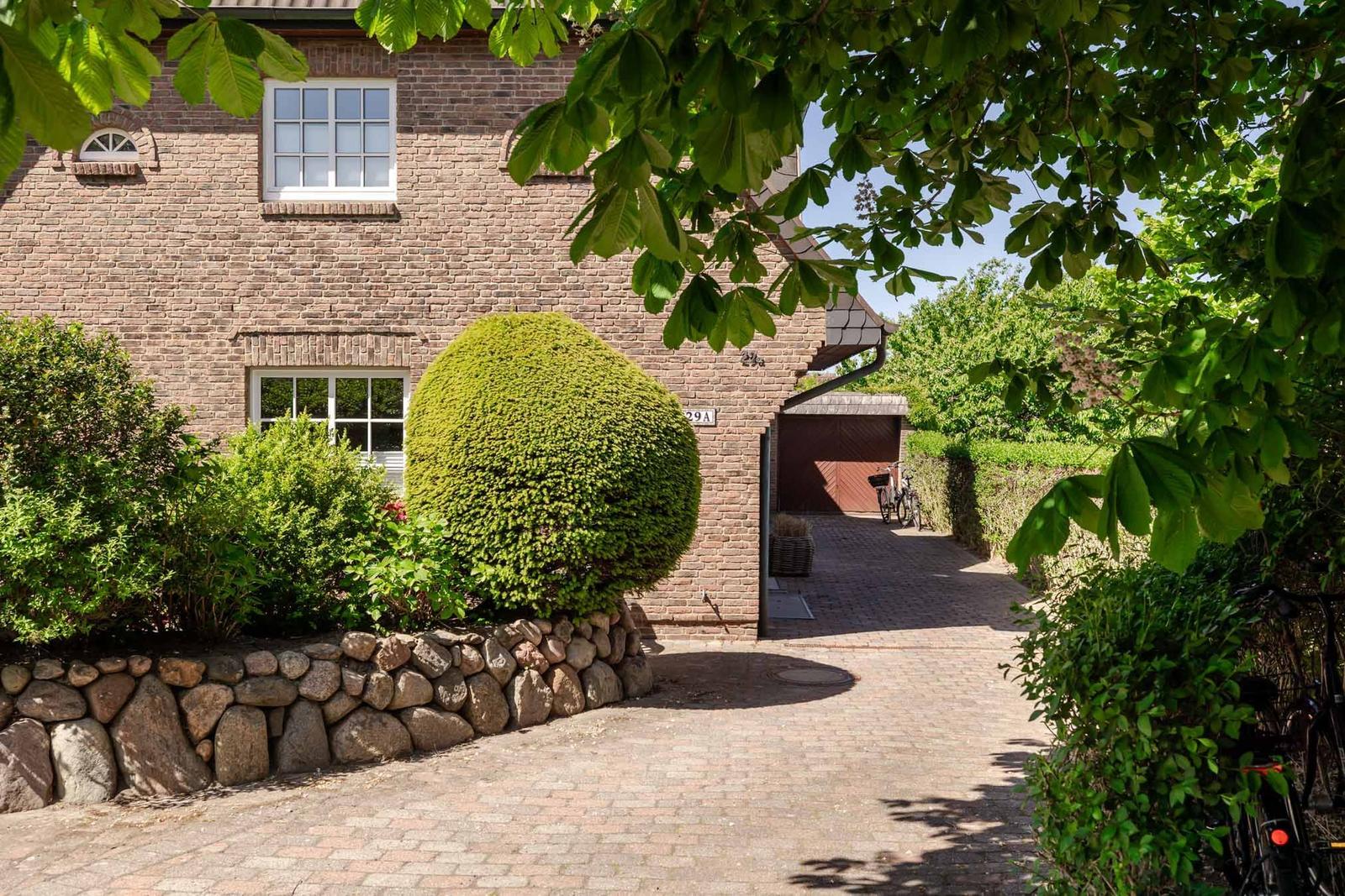 House with stone wall, manicured garden bed, and gravel path. Bicycles are in the back yard.