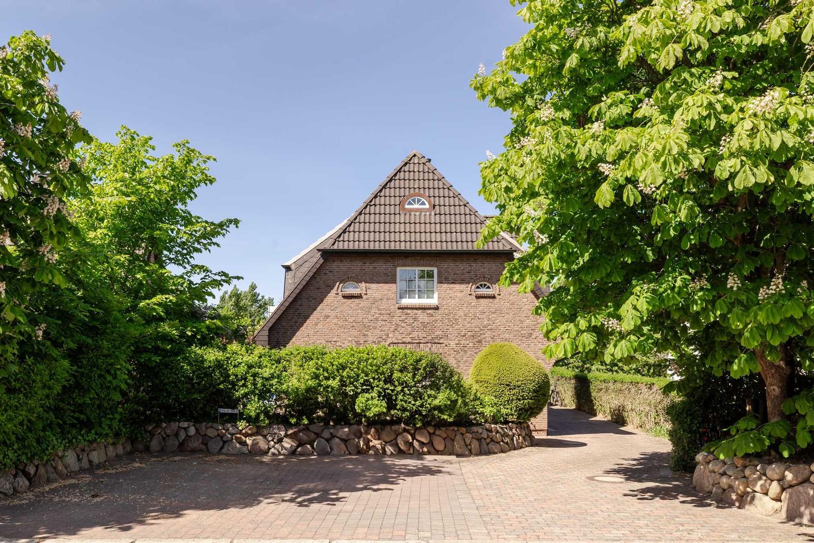 House with brick facade, slate roof, and landscaped garden. Stone wall and trees surround the entrance.