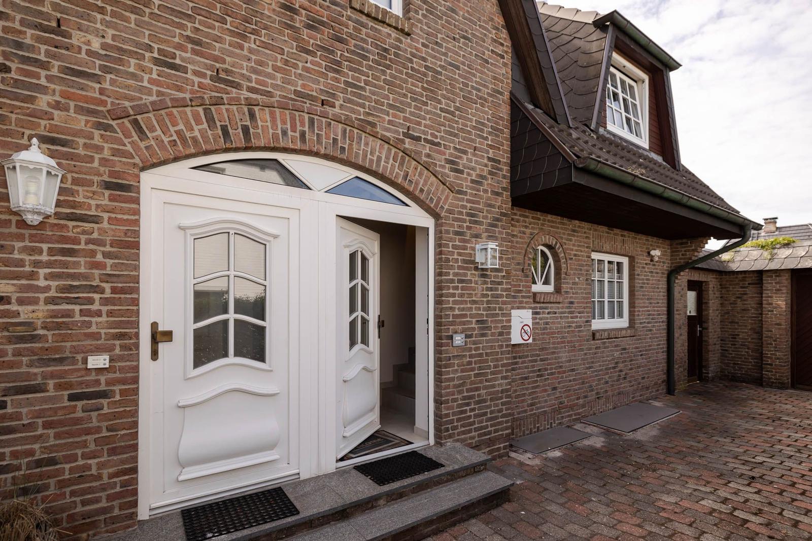 House with red brick, white entrance door, and dormer window.