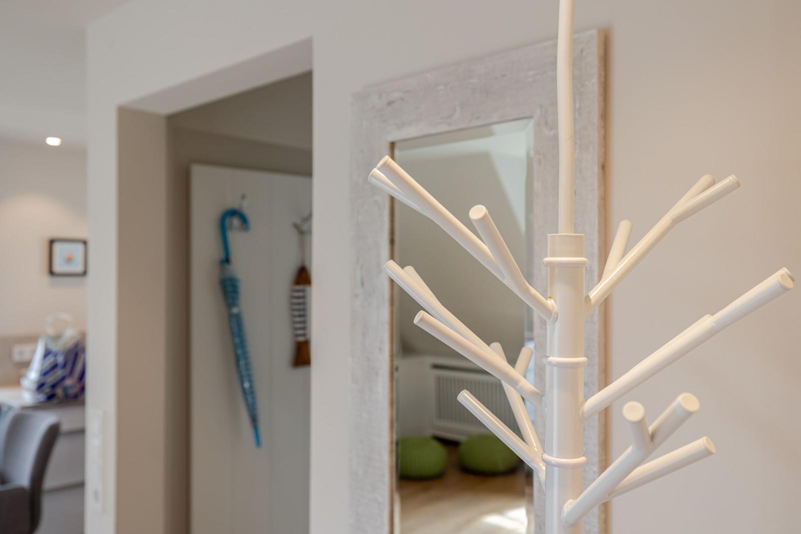 White coat rack with branches, mirror in background, blue umbrella on wall.