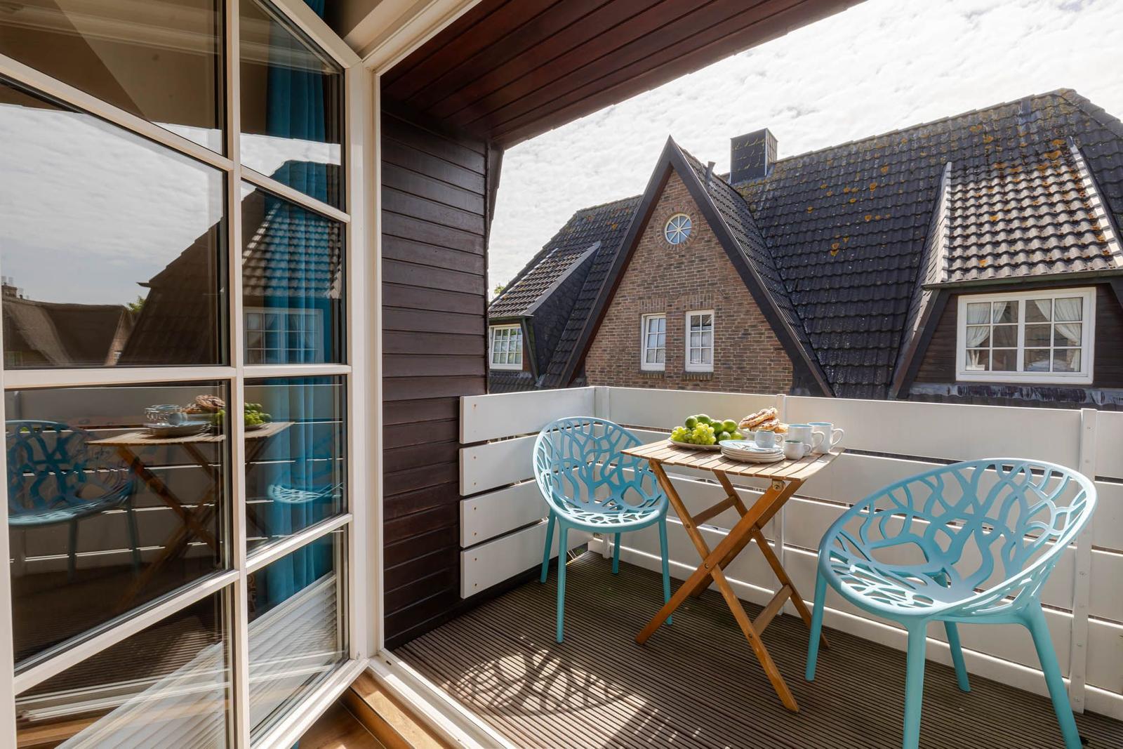 Terrace with table and two blue chairs. View of rooftops and house facades.