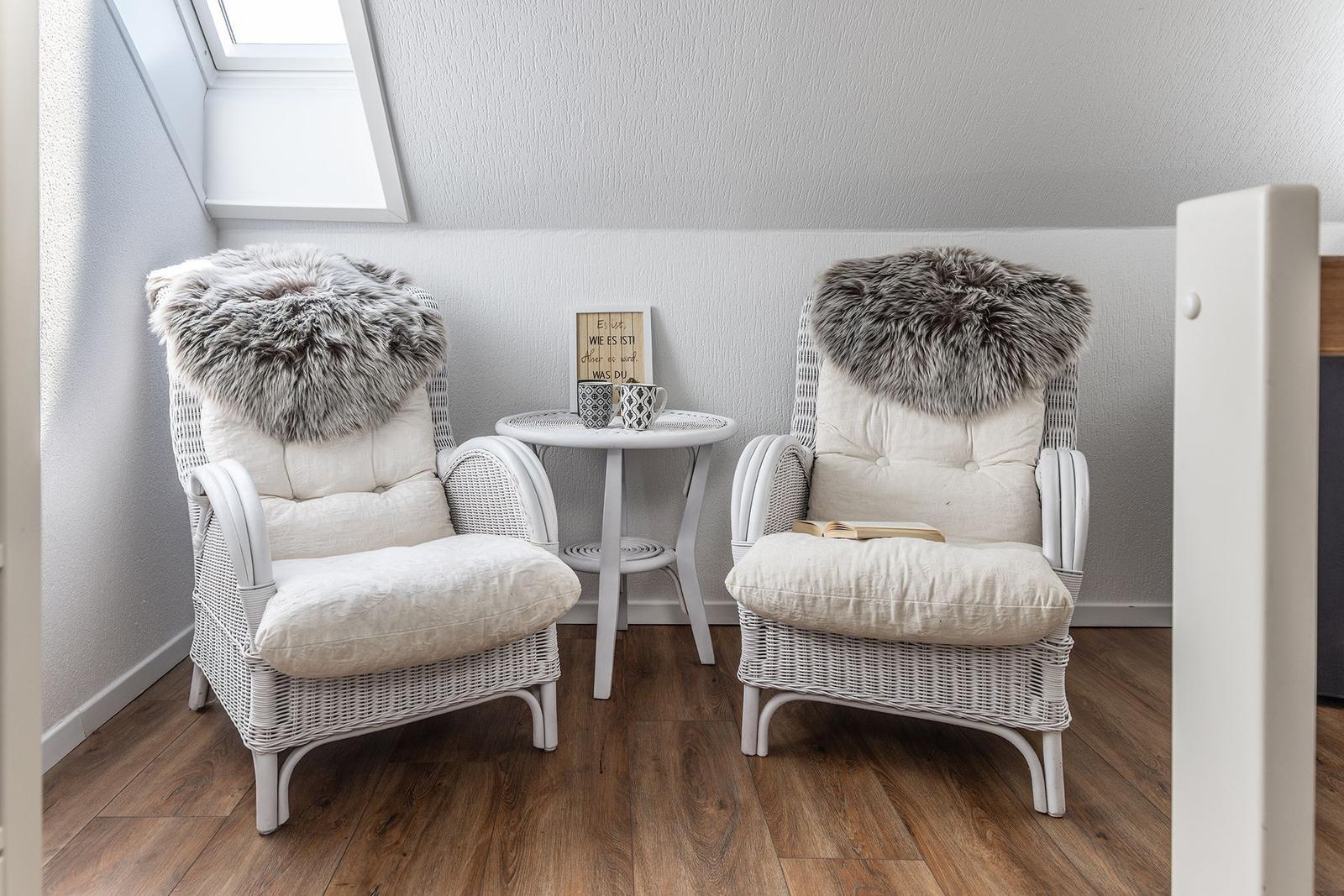 Zwei weiße Rattan-Stühle mit Fellkissen und einem Tisch dazwischen.