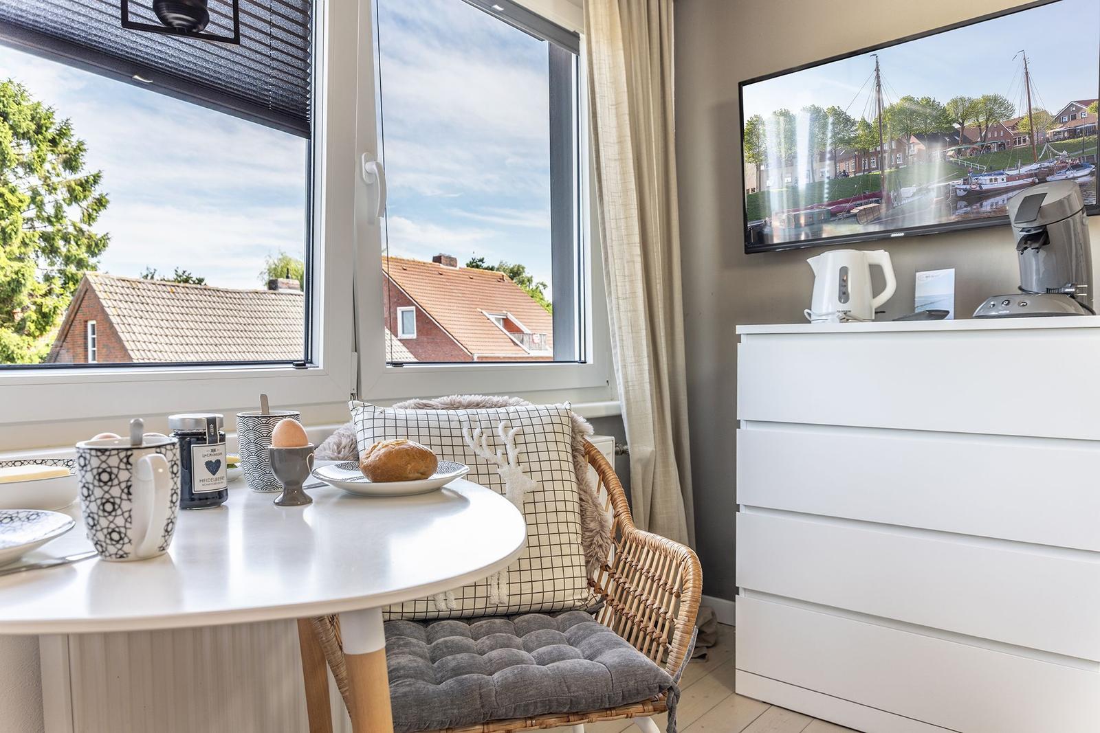 Tisch mit Frühstück und Sessel vor Fenster mit Blick auf Dächer.