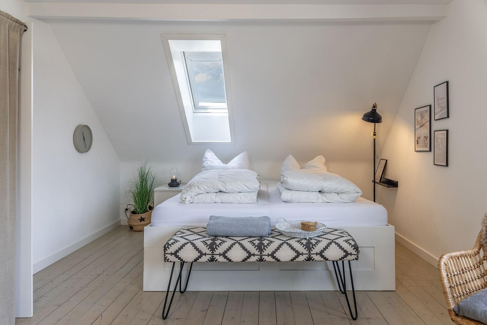 Schlafzimmer mit Dachschrägen, Dachfenster, Bett und Bank.
