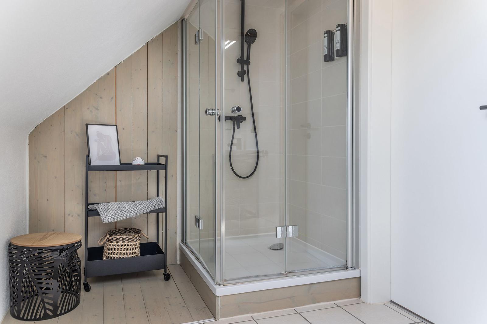Duschkabine mit Glaswand, Holzwand und Regal mit Handtuch.